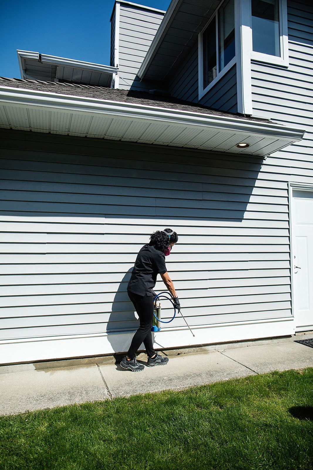 A woman is cleaning the side of a house with a pressure washer.