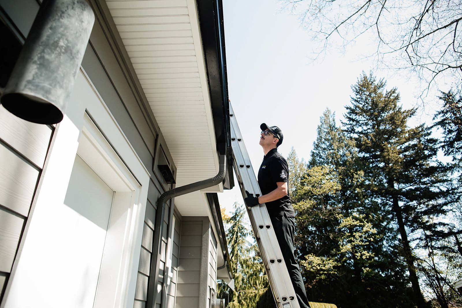 A man is standing on a ladder working on the gutters of a house.