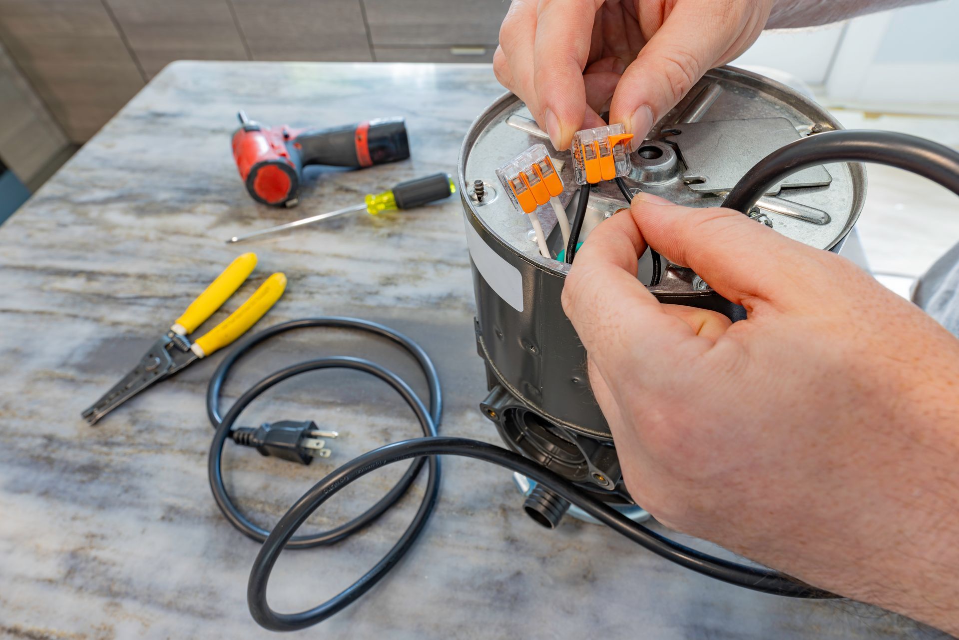 Hands repairing a black appliance with wires and tools on a workbench