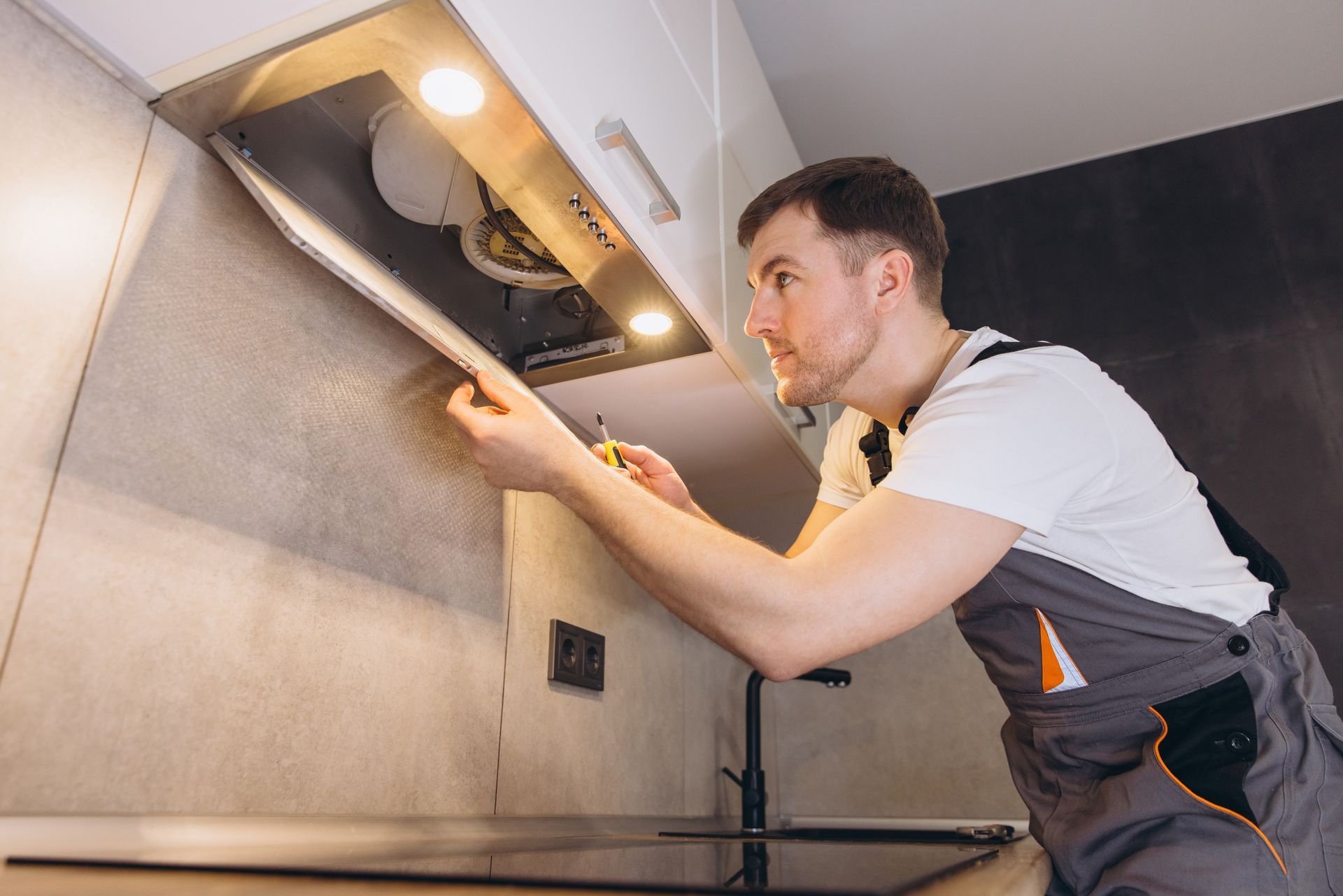 Technician inspecting an under-cabinet range hood in a kitchen with a flashlight