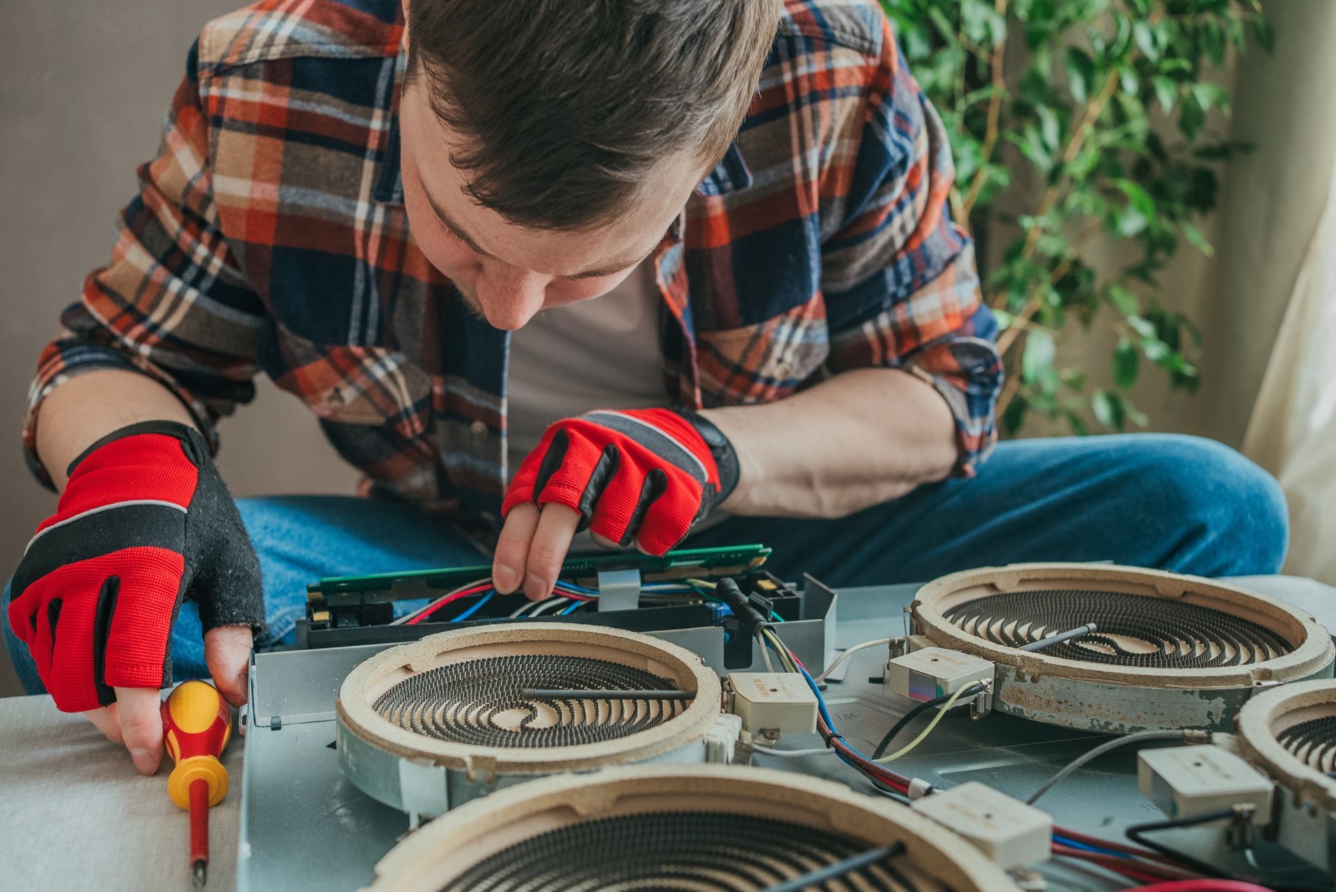 Person in red gloves repairing electronic equipment with a screwdriver on a workbench