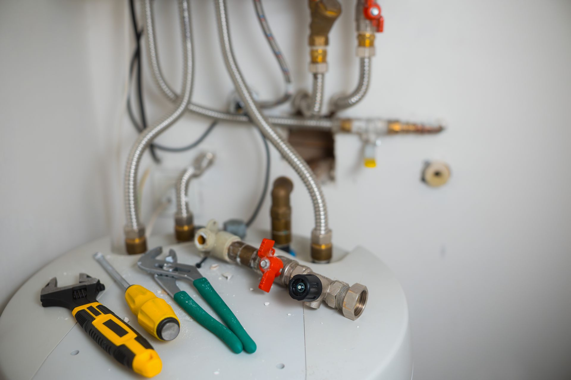 Plumbing tools on a white sink under exposed pipes and fittings in a bathroom or utility area