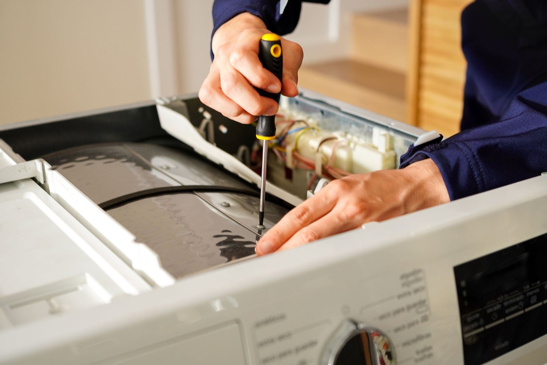 Technician repairing the open top of a white appliance with a screwdriver and tool.