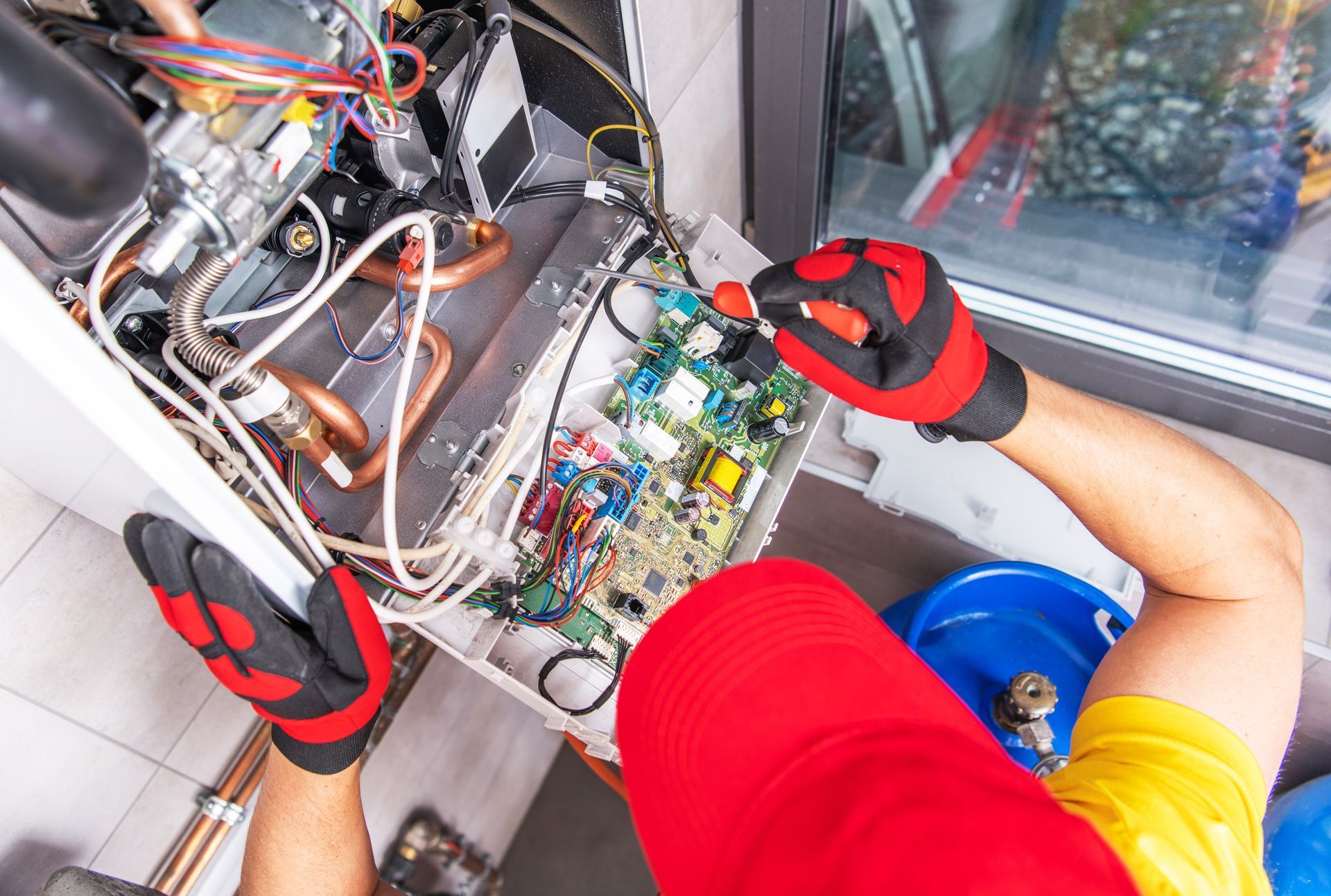 Technician in red gloves working on exposed electrical panel beside a window