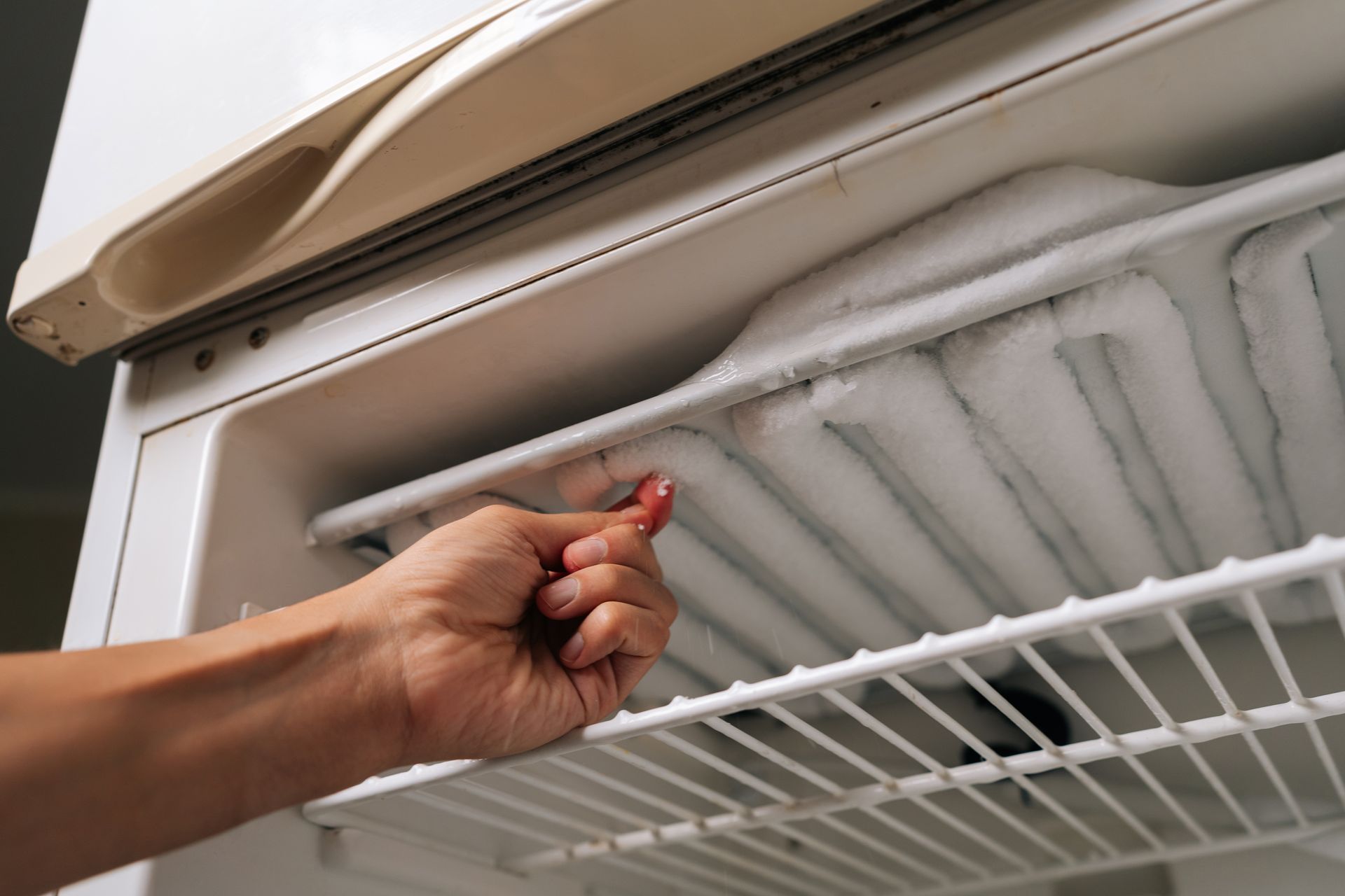 Hand reaching into a freezer to lift a frosted shelf panel