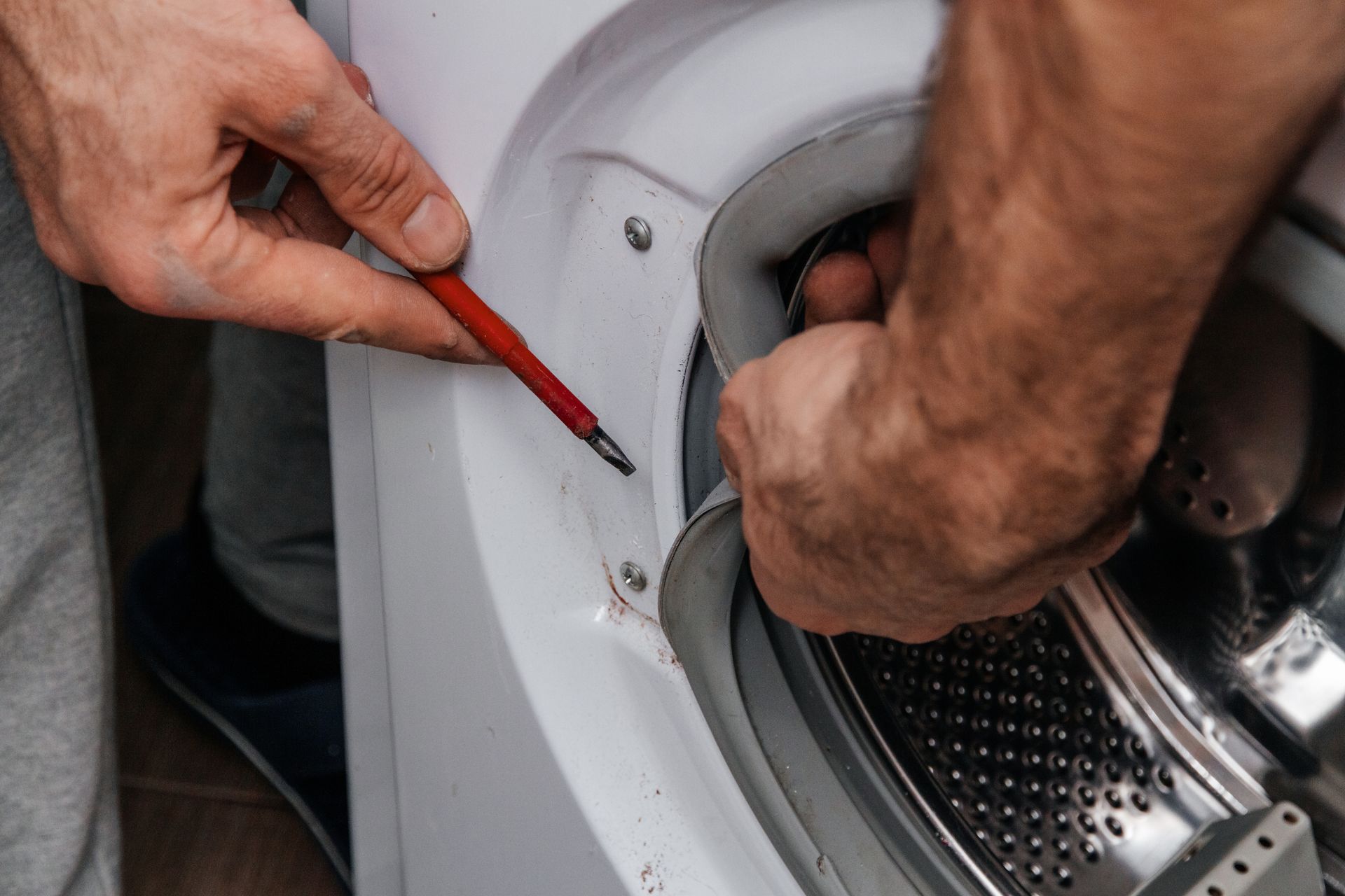 Hands using a red screwdriver to adjust the door seal on a white front-loading washing machine.
