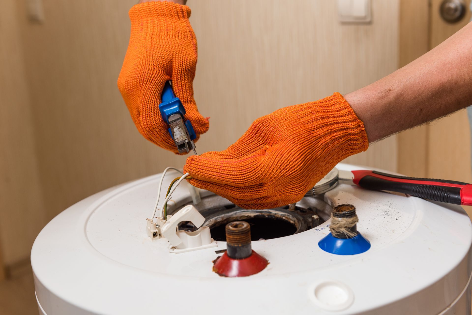 Gloved hands wiring the top of a white water heater with red and blue valve knobs