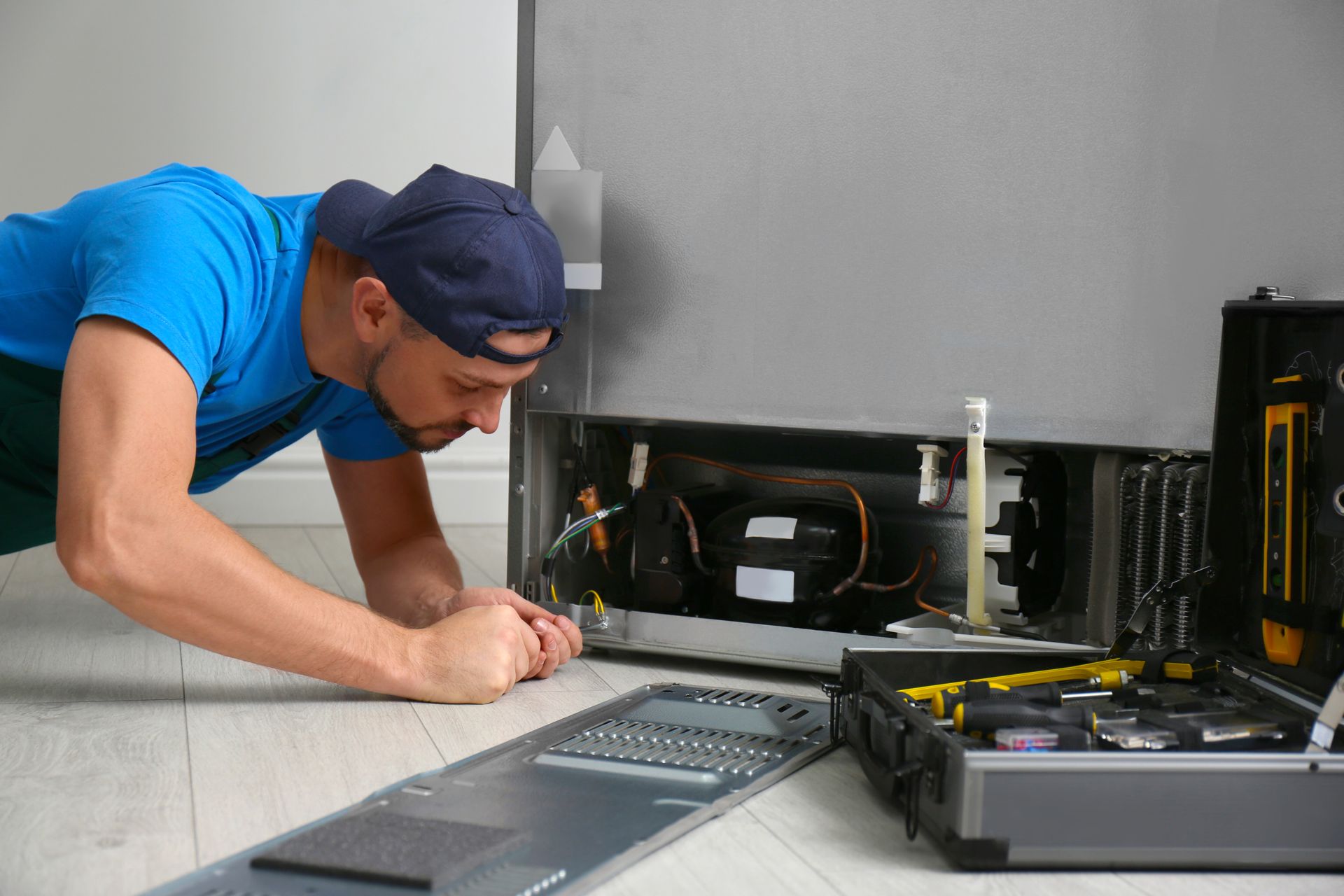 Technician in blue shirt and cap repairing an open computer with tools on a workbench.