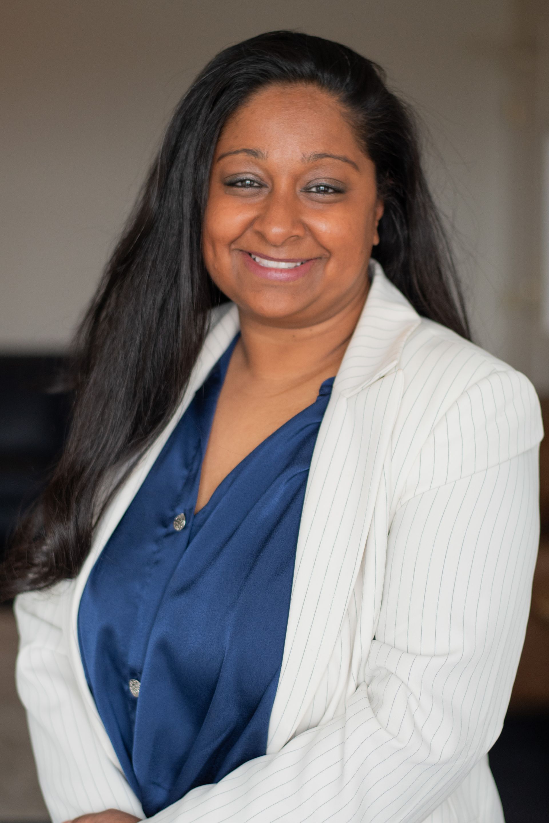 Woman in gray pinstripe suit, standing on a wooden balcony, smiling. Modern, open-concept office.