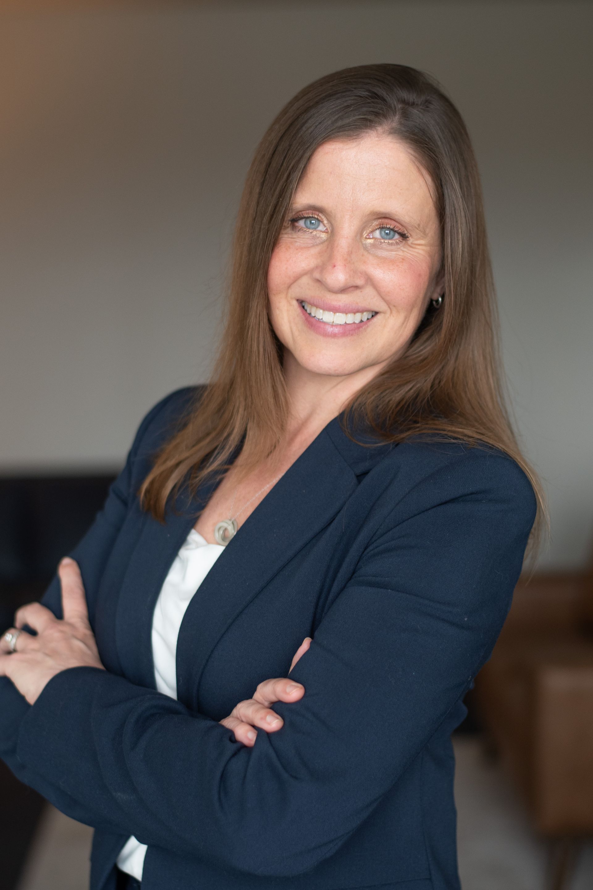 Woman in a light suit smiles, leaning on a railing inside a modern building with high ceilings.