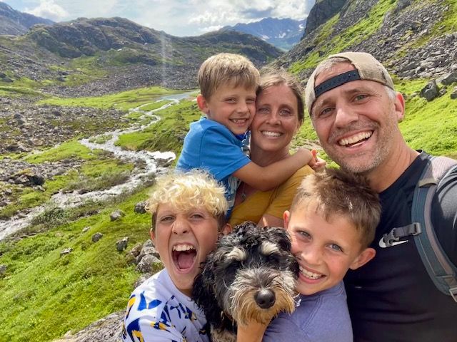 Family selfie in mountain landscape, smiling with dog.