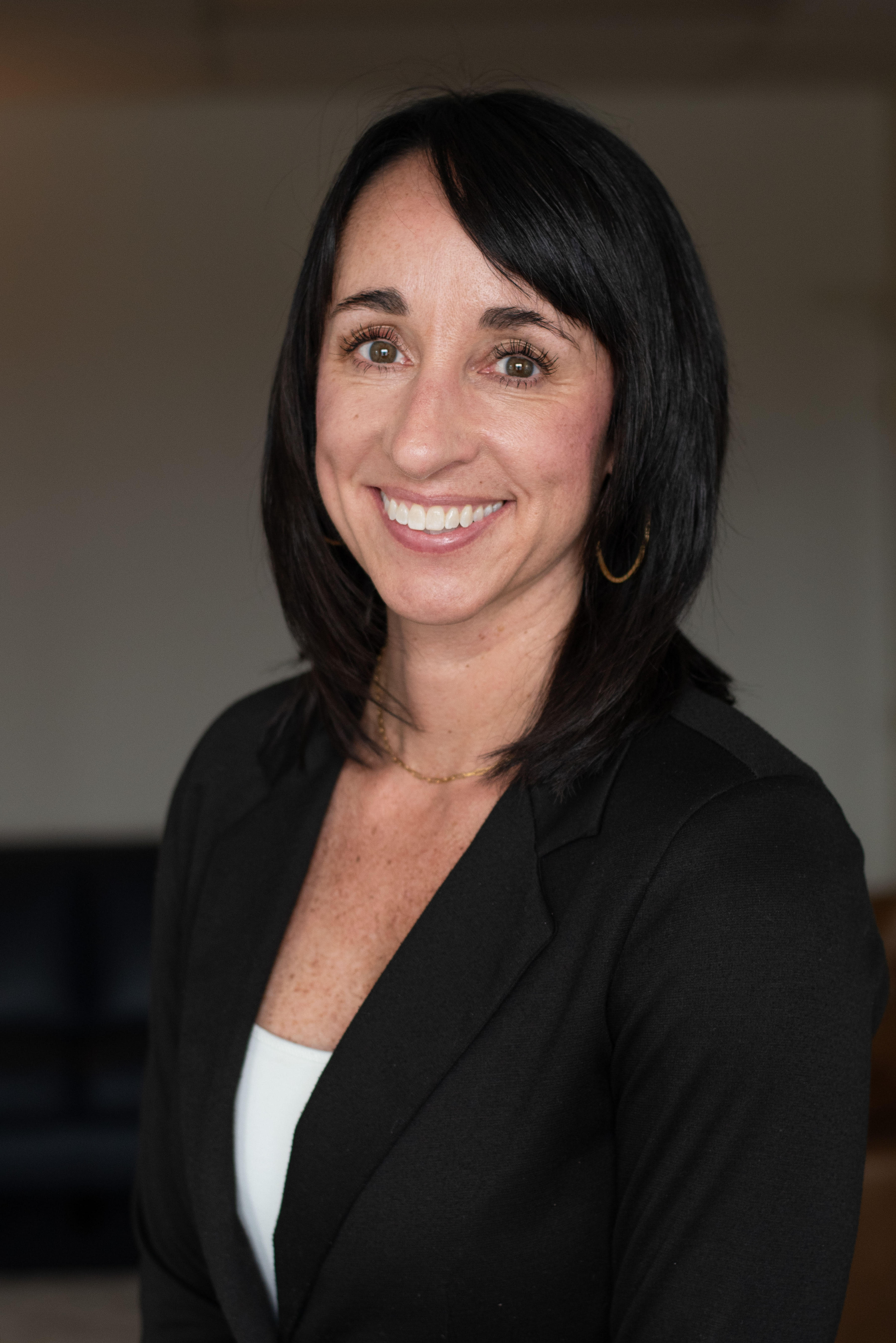 Woman in a light suit smiles, leaning on a railing inside a modern building with high ceilings.