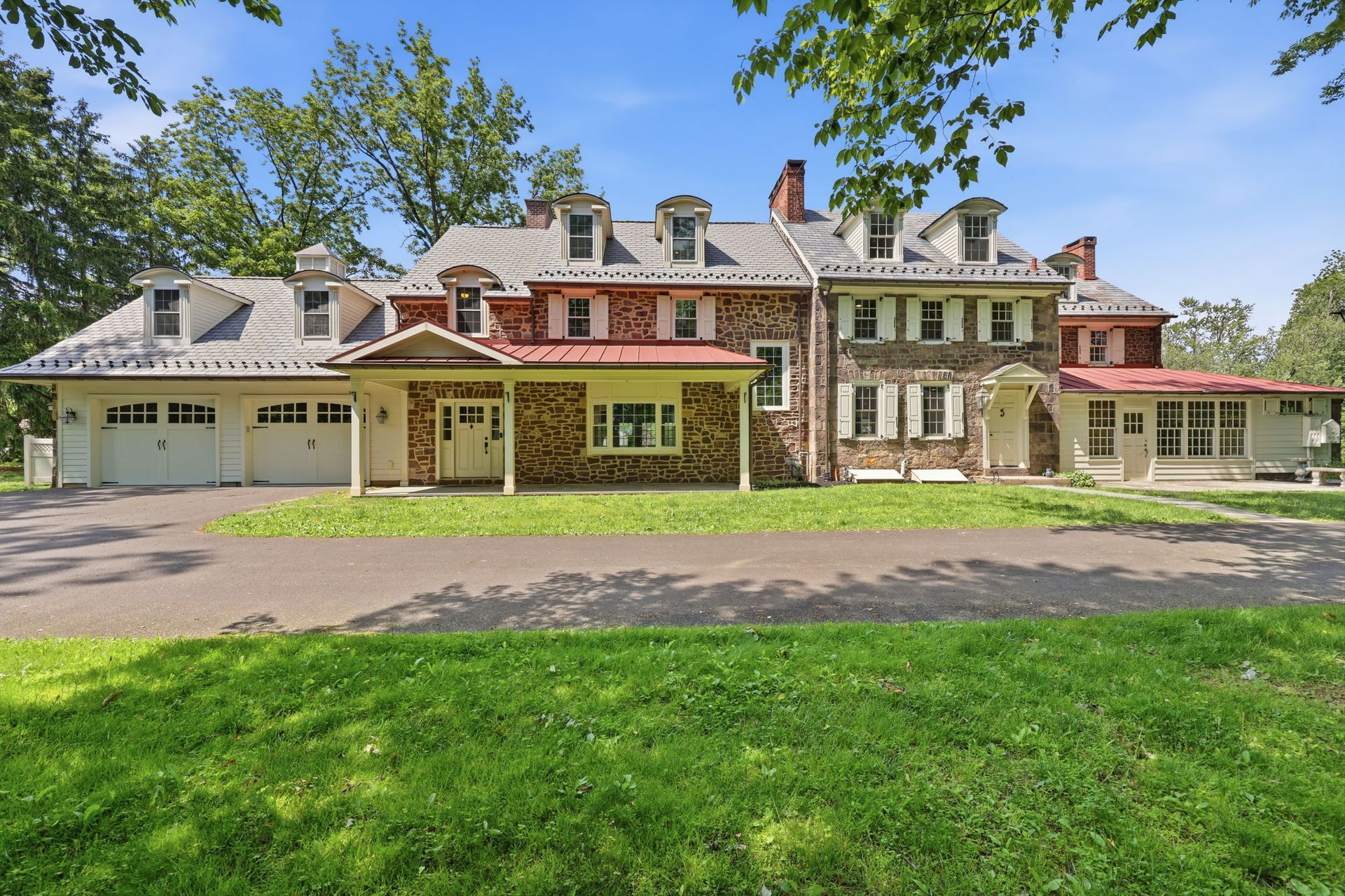 Large stone mansion with red roofs, front driveway, and green lawn under a blue sky