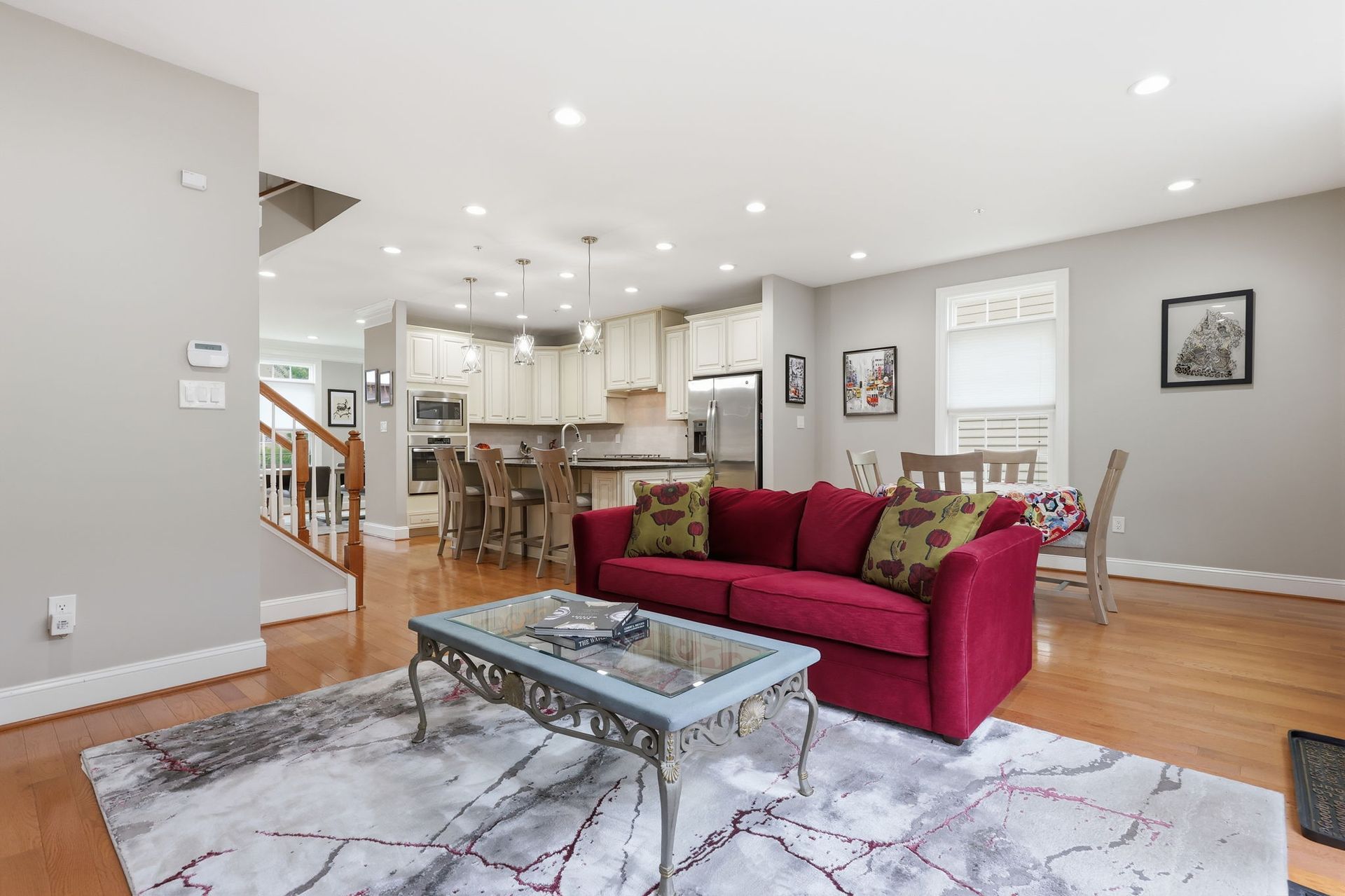Bright open living room with red sofa, coffee table, stairs, and kitchen in the background