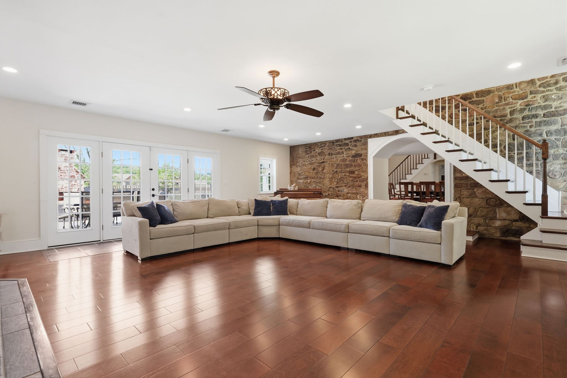 Spacious living room with sectional sofa, hardwood floors, exposed brick, and staircase to upper level