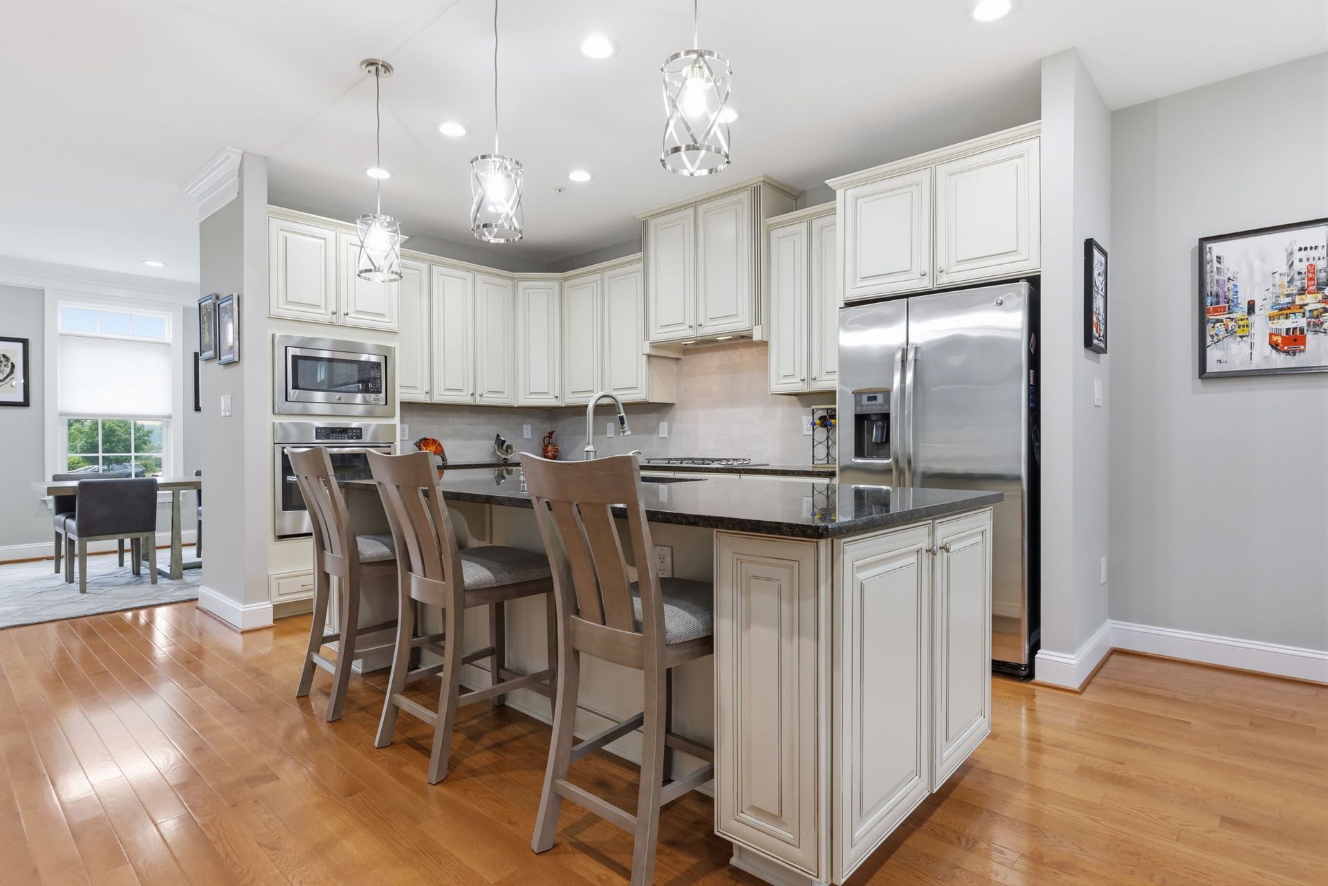 Bright modern kitchen with white cabinets, stainless appliances, island stools, and hardwood floors