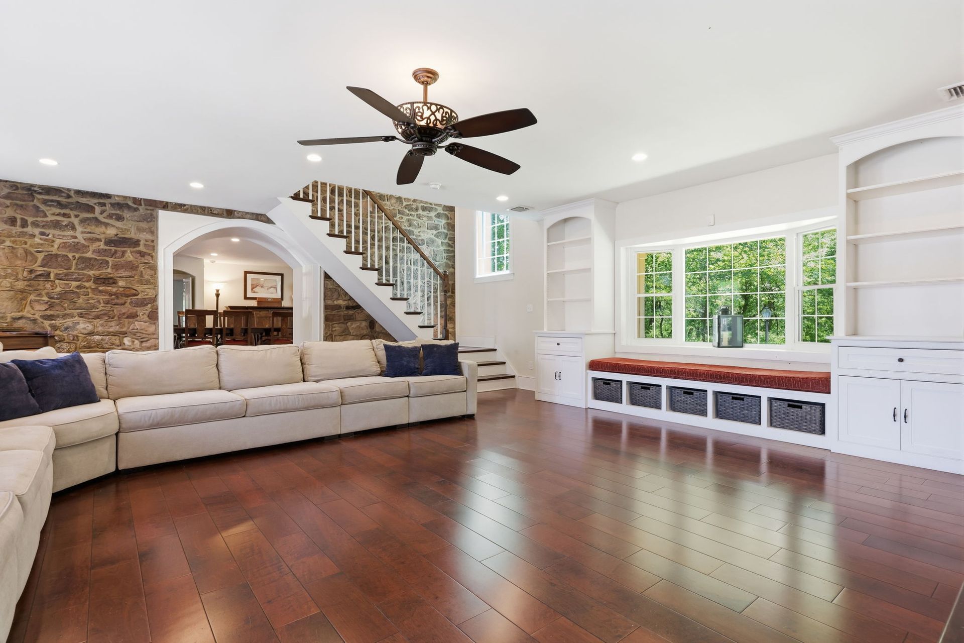 Spacious living room with sectional sofa, dark wood floors, staircase, ceiling fan, and built-in window seating