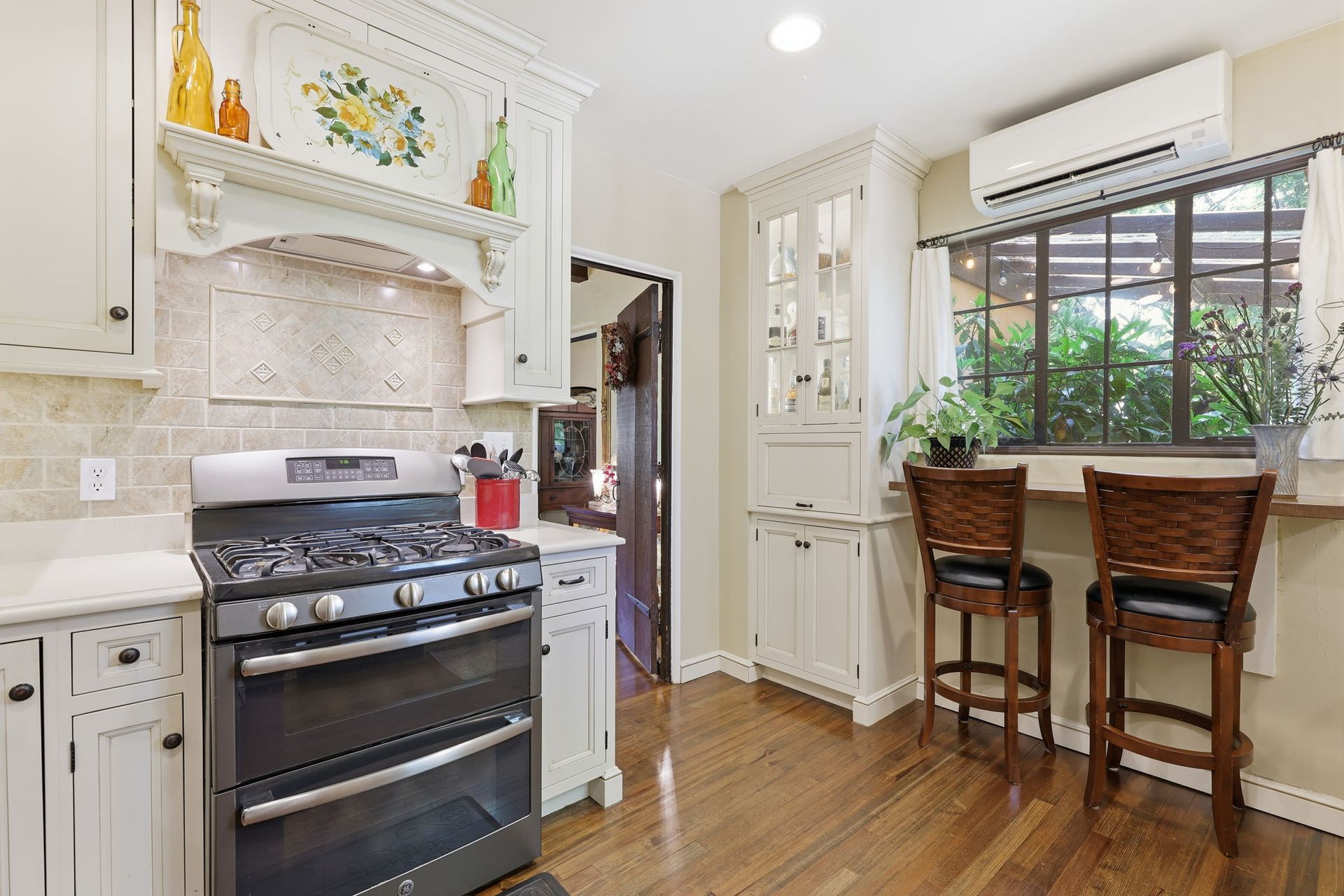Bright kitchen with white cabinets, marble counters, black stove, and two wooden stools by a window.
