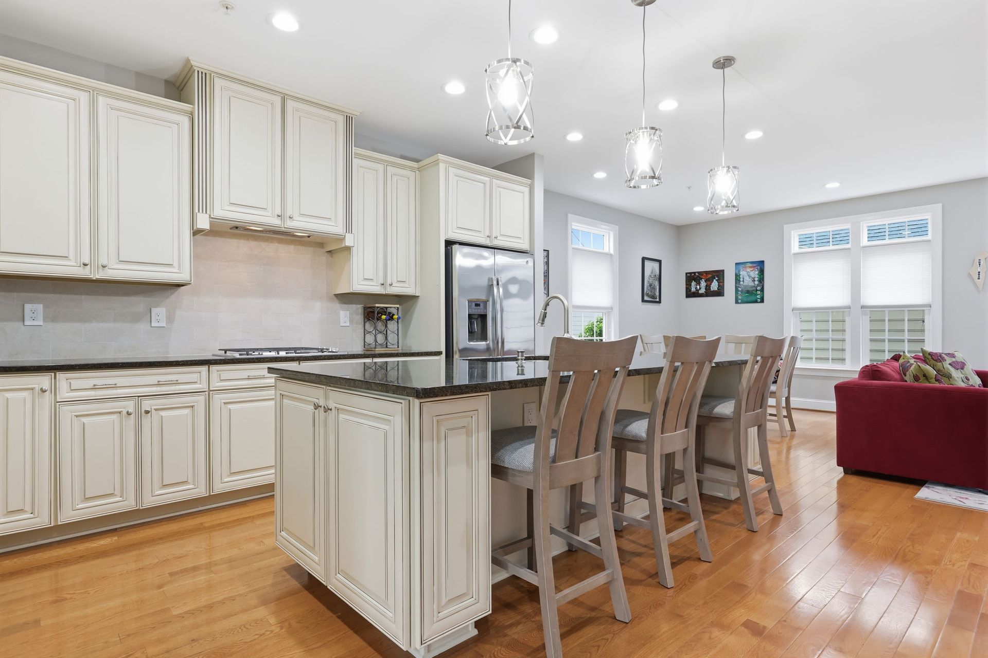 Bright white kitchen with island, barstools, stainless fridge, hardwood floors, and adjacent living area with red sofa
