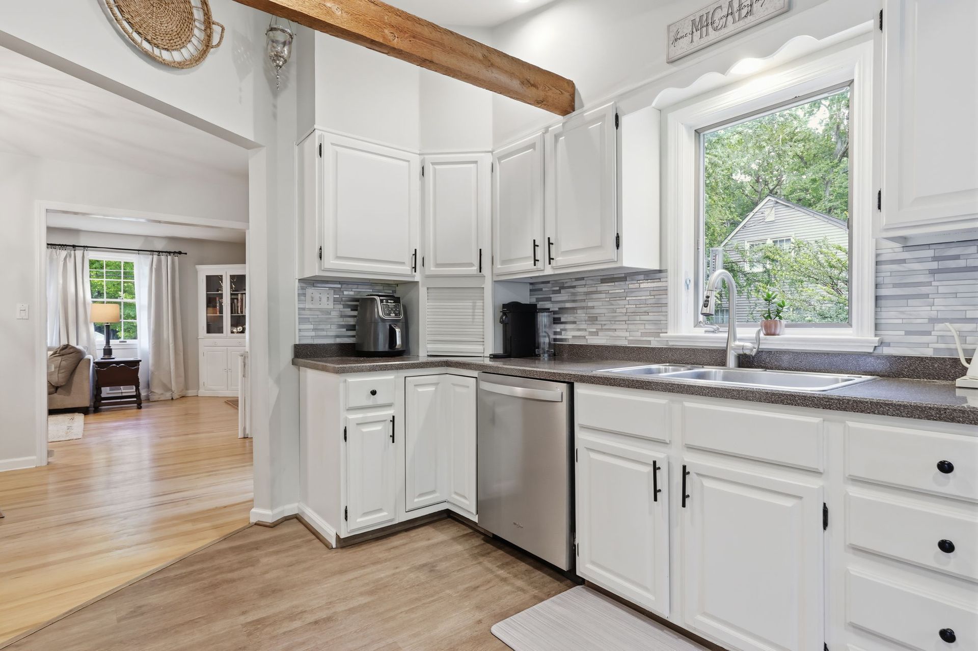 Bright white kitchen with stainless appliances, marble countertops, and a window over the sink