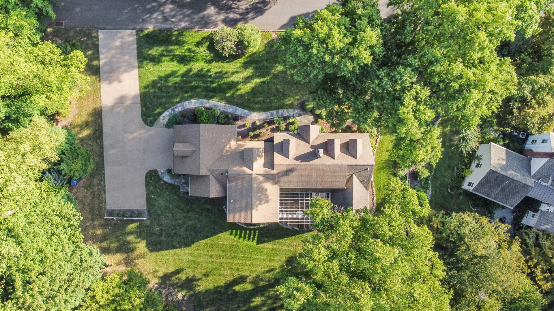 Aerial view of a house with a driveway surrounded by trees and grass on a sunny day.
