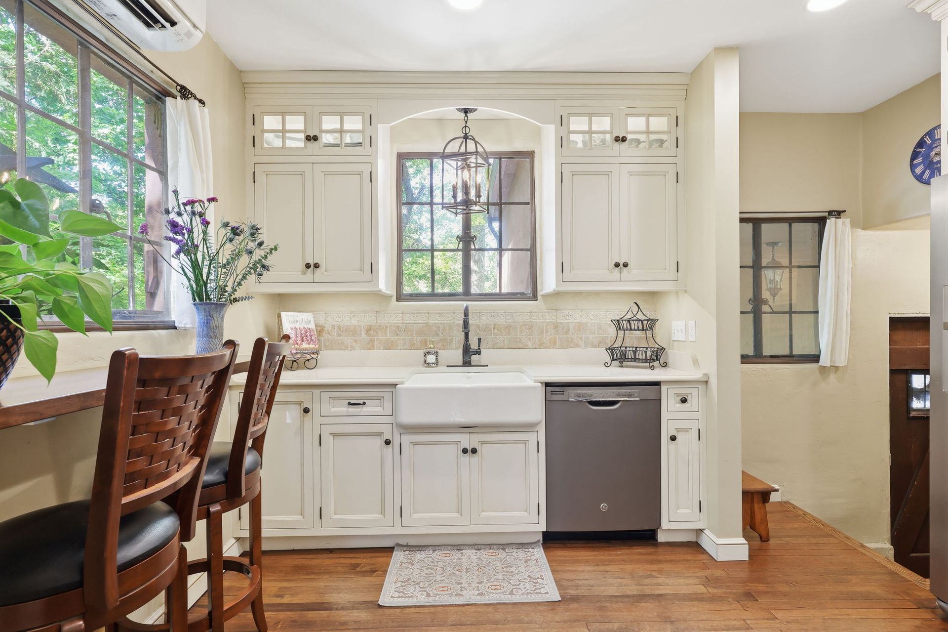 Bright kitchen with white cabinets, wood floor, dining table, sink window, and stainless dishwasher