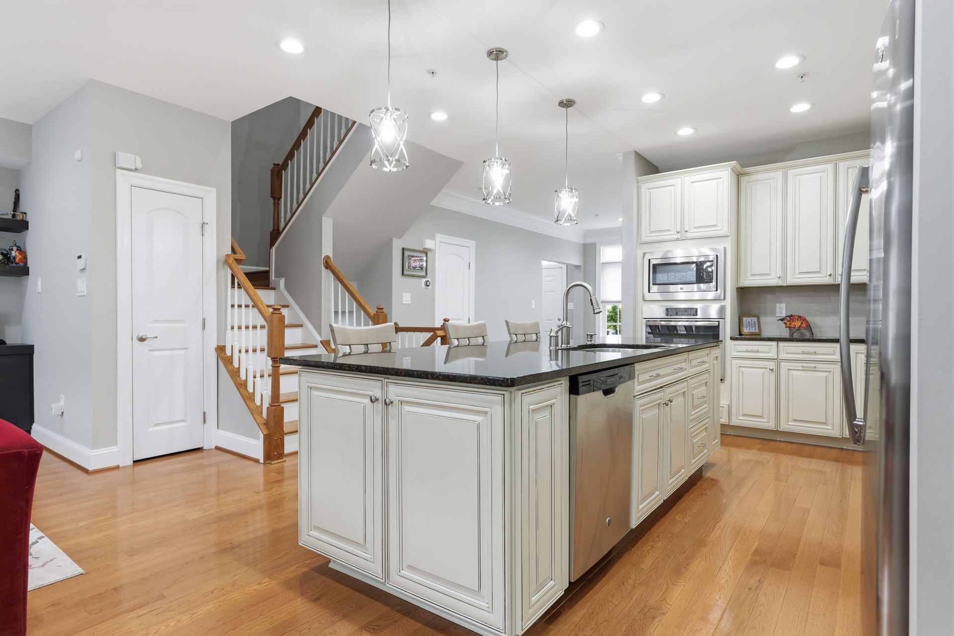 Bright modern kitchen with white cabinets, black granite island, hardwood floors, and staircase nearby