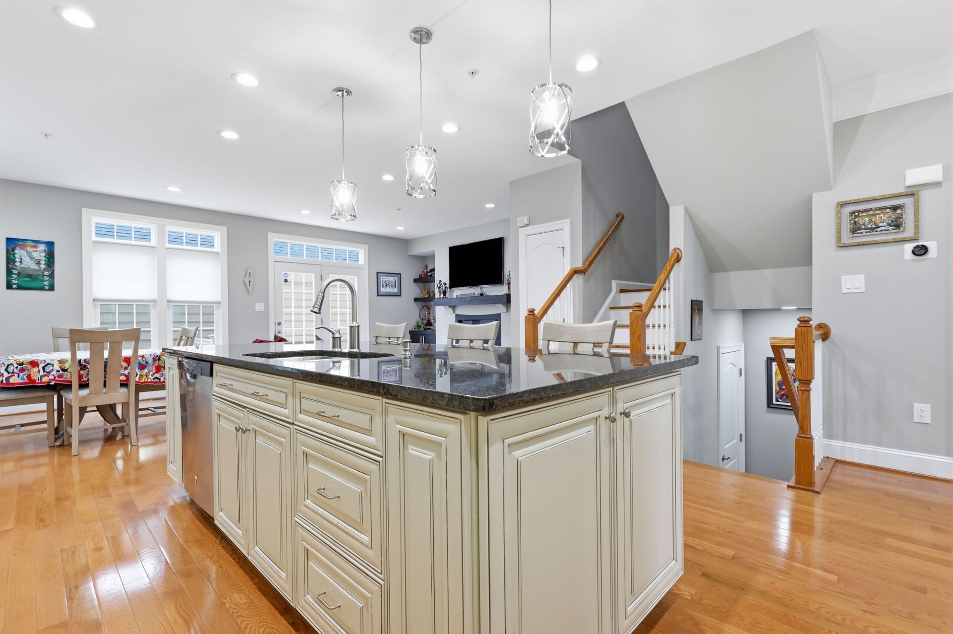 Bright modern kitchen with large island, light wood floors, and staircase in the background