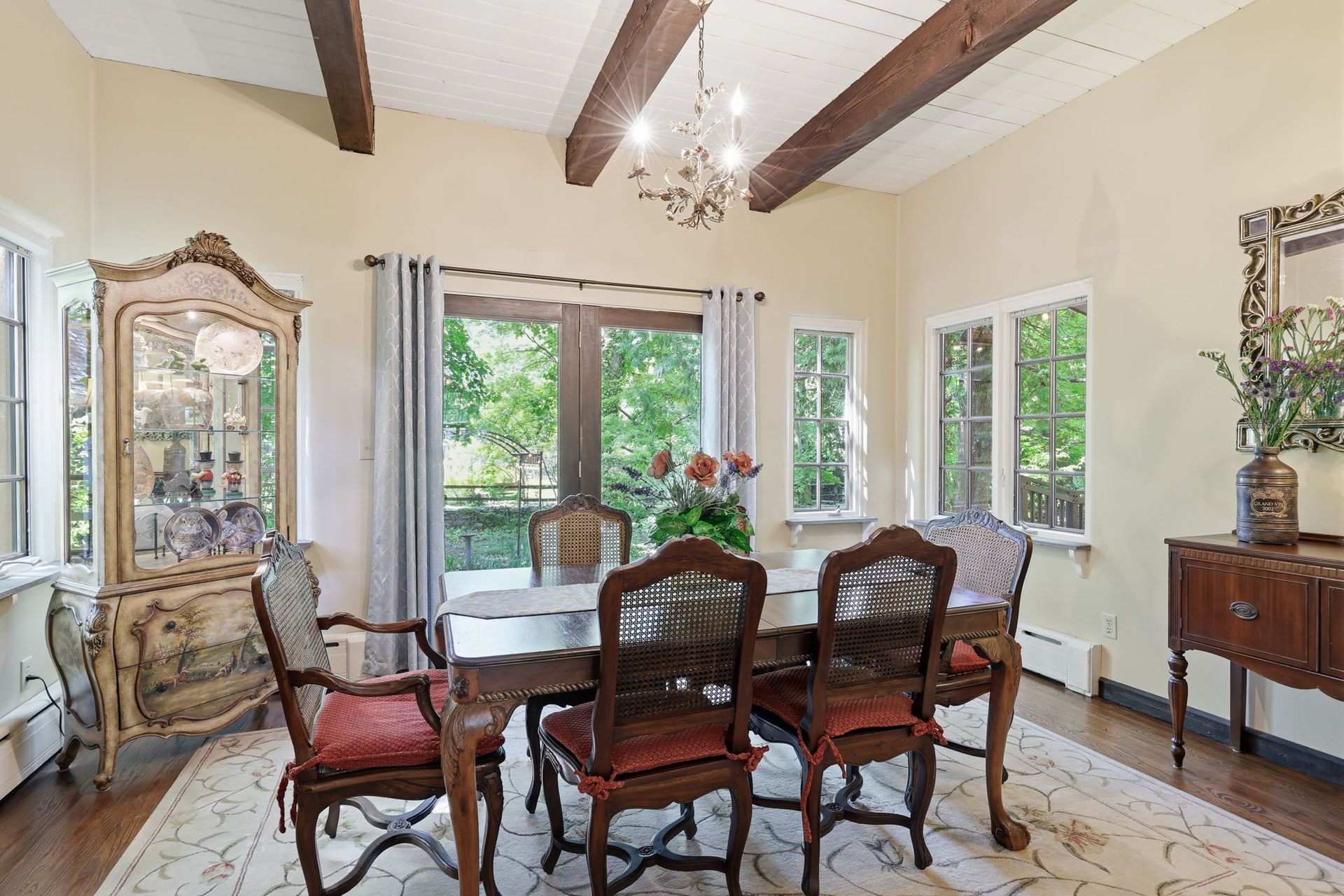 Bright dining room with glass table, ornate chairs, large windows, and chandelier