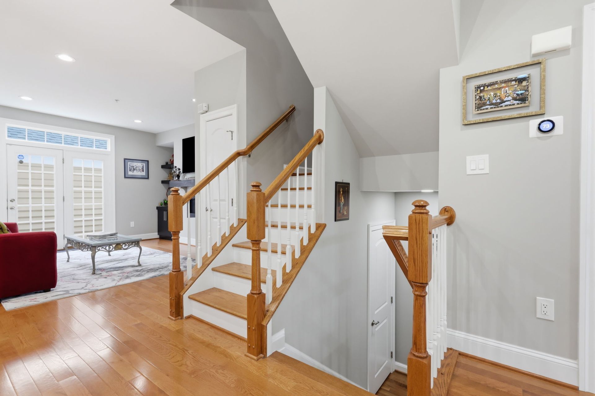 Bright foyer with wooden staircase, white walls, hardwood floors, and a living room visible to the left