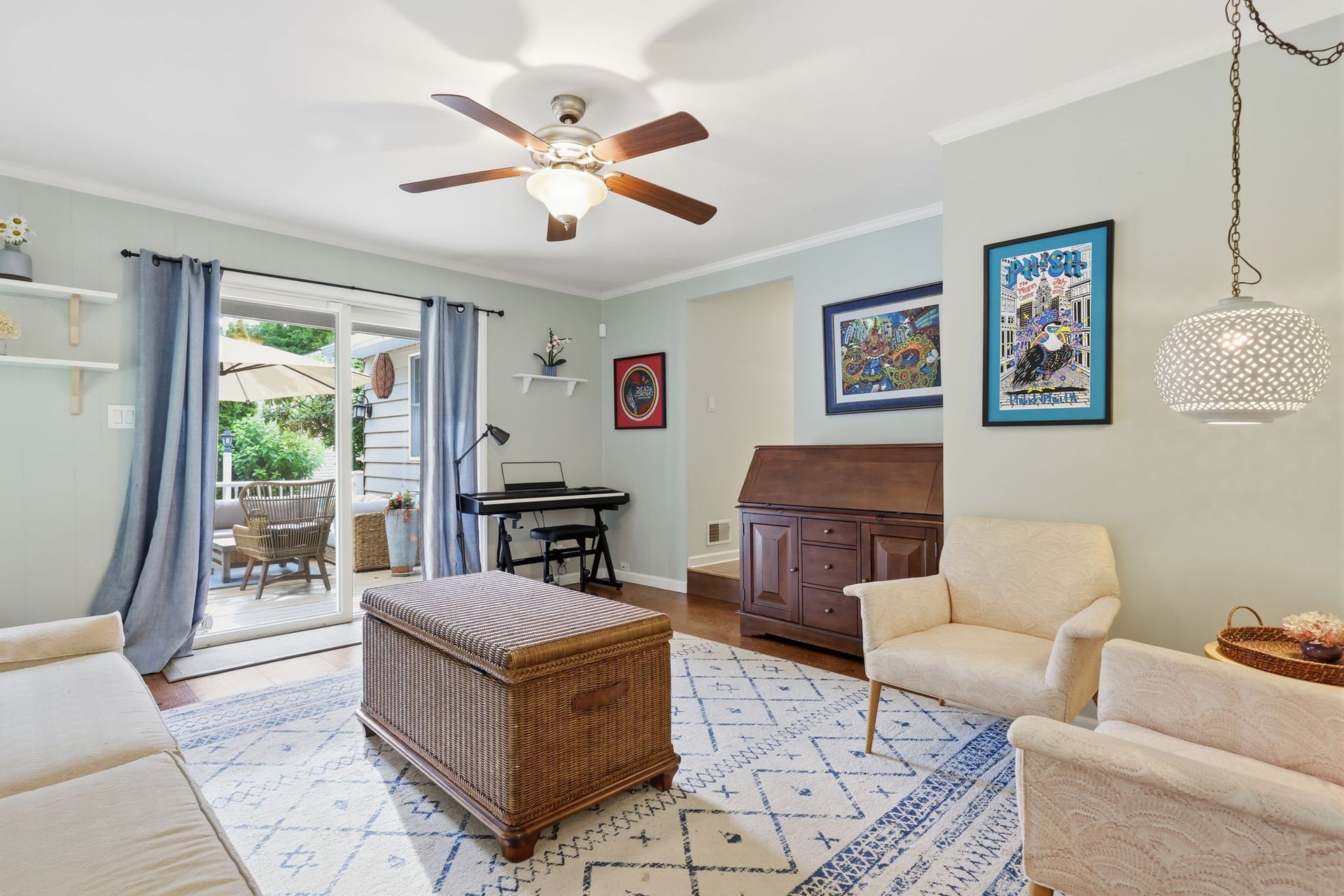 Bright living room with wicker coffee table, cream chairs, piano, and open sliding door to patio