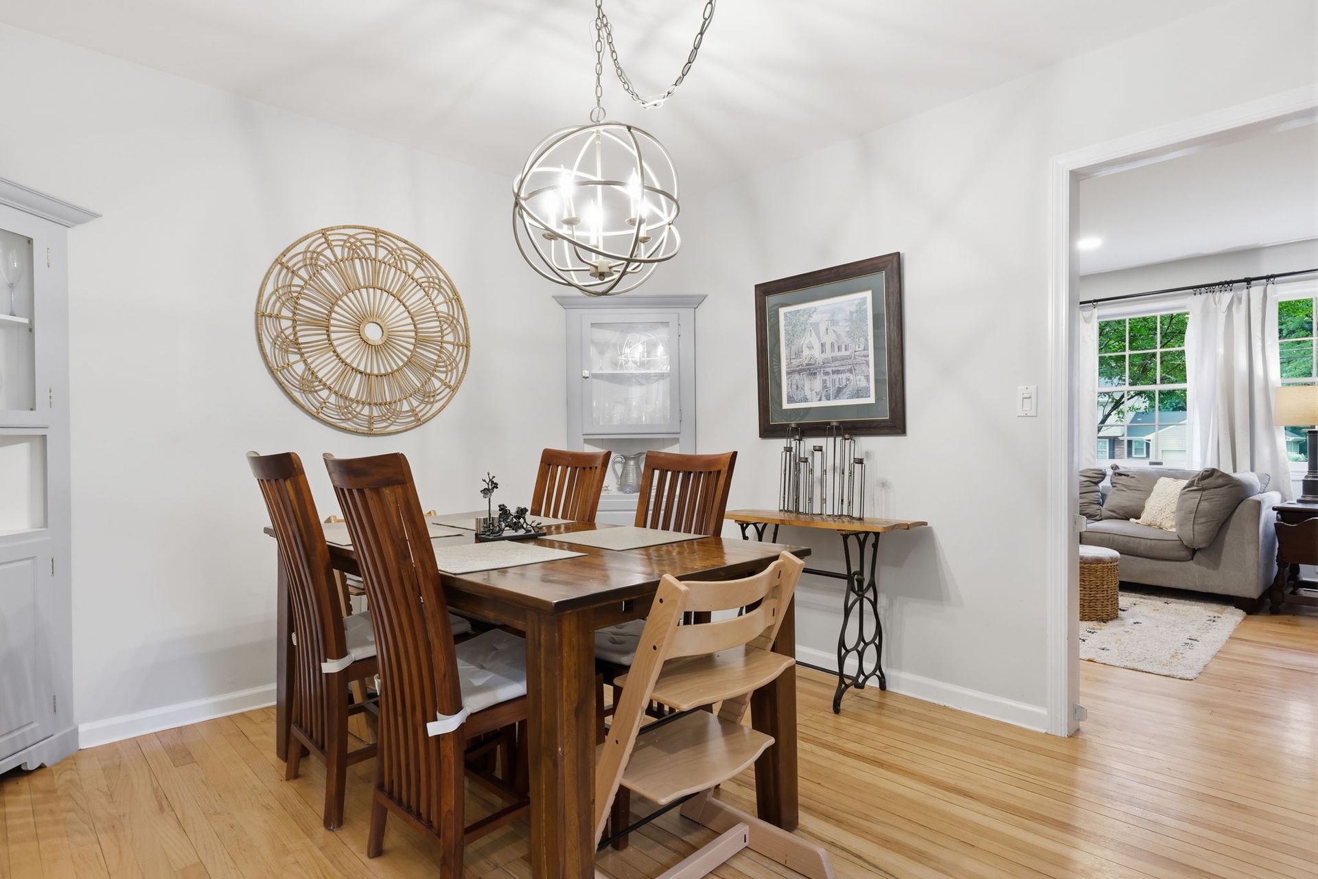 Dining room with wooden table and chairs, gold wall art, and an adjoining living room visible through the doorway.