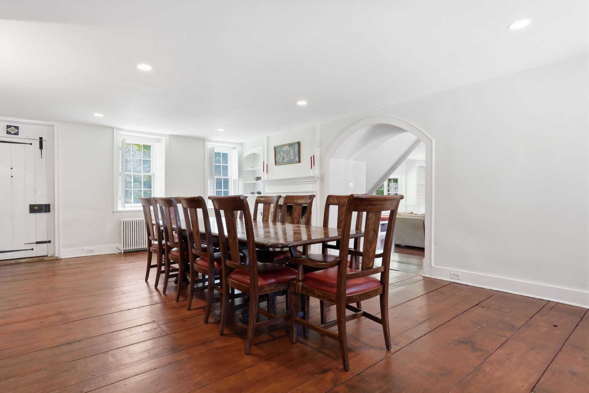 Bright dining room with long wooden table, chairs, and white walls, lit by recessed ceiling lights