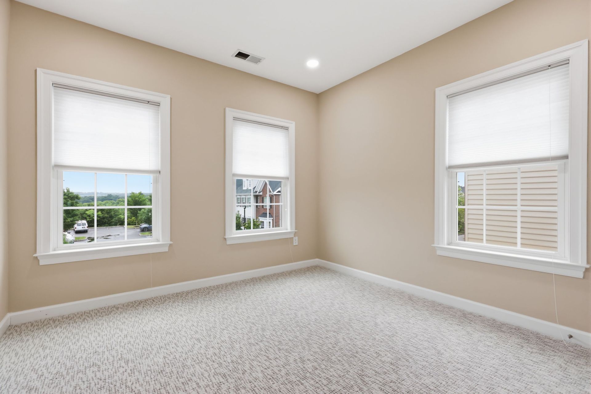 Empty beige room with carpet, three windows, and white trim under recessed ceiling lights