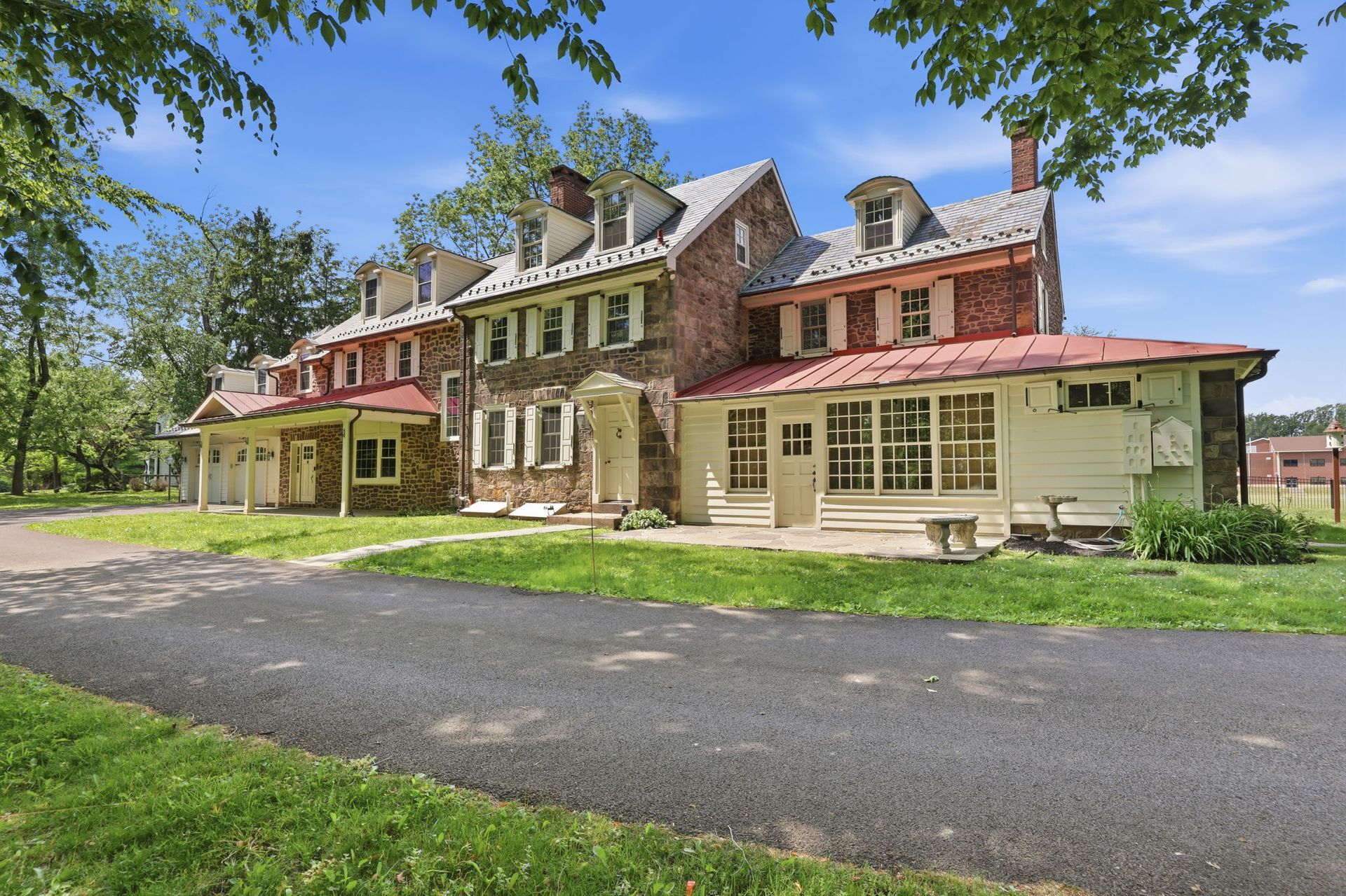 Large historic house with cream siding and red roofs beside a driveway under sunny trees