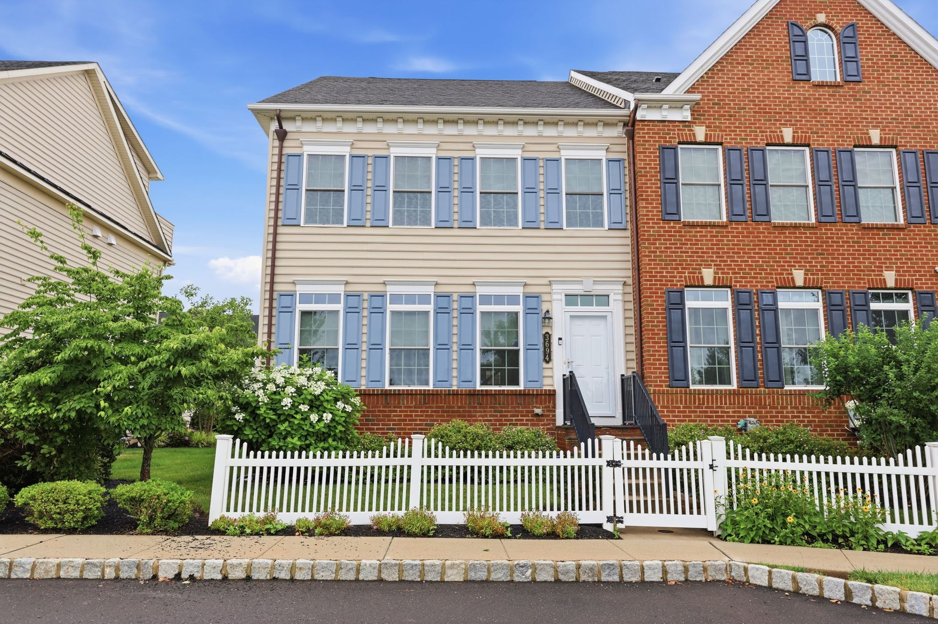 Two-story brick homes with white fences and front gardens on a sunny street