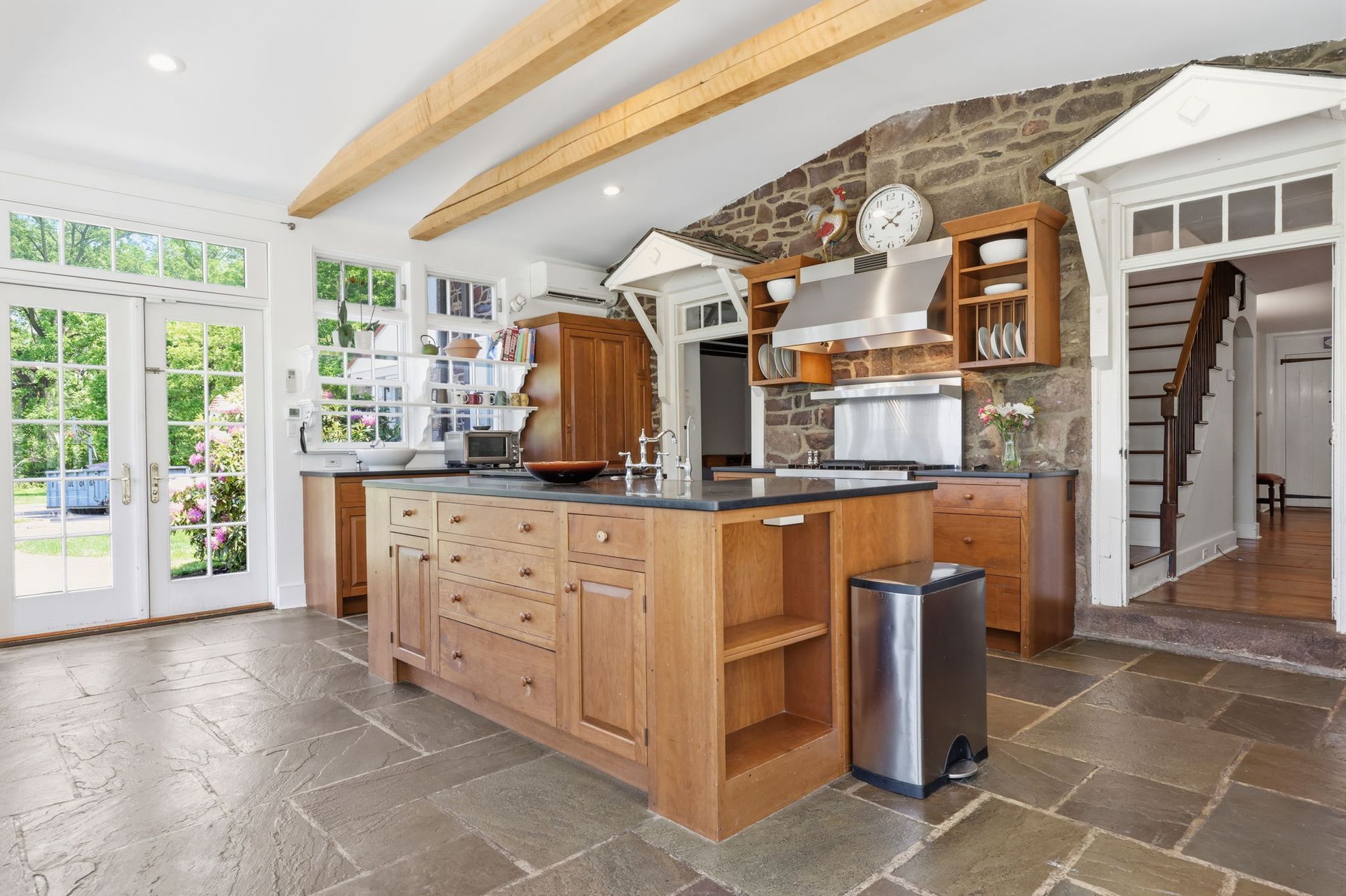 Bright rustic kitchen with wood island, stone backsplash, and large windows opening to greenery
