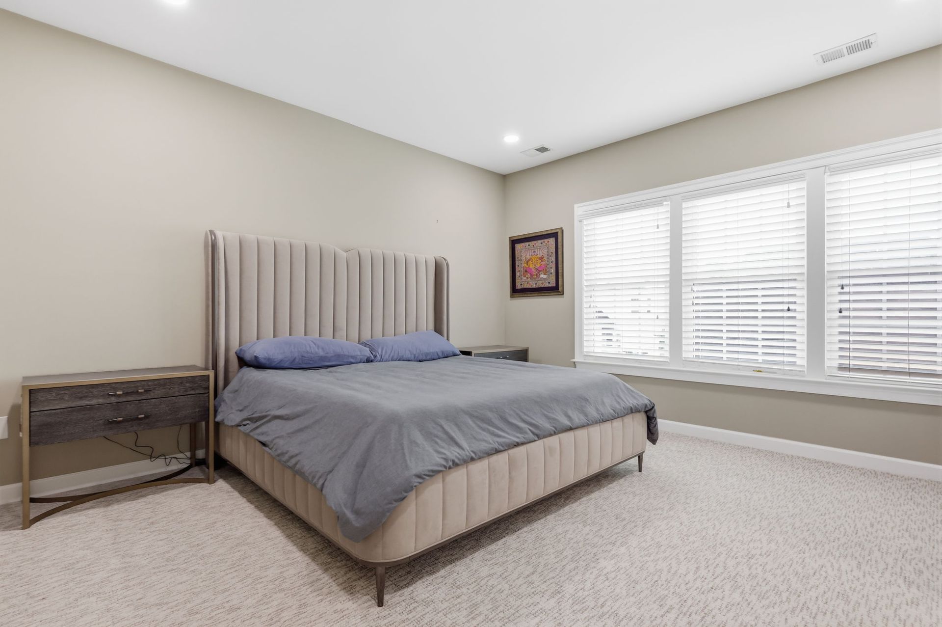 Modern bedroom with a bed, nightstand, gray bedding, and large window blinds.