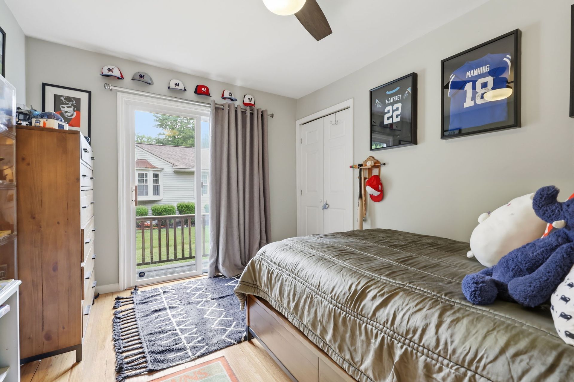 Small bedroom with a bed, jersey wall decor, open balcony door, and sunlight streaming in.