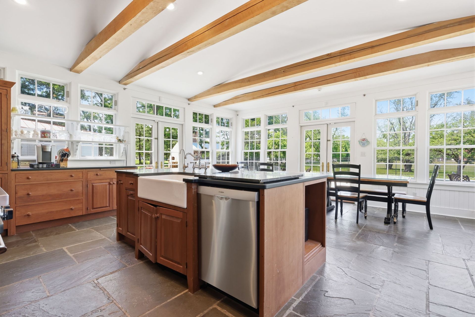 Bright modern kitchen with wood beams, large windows, island, and dining table