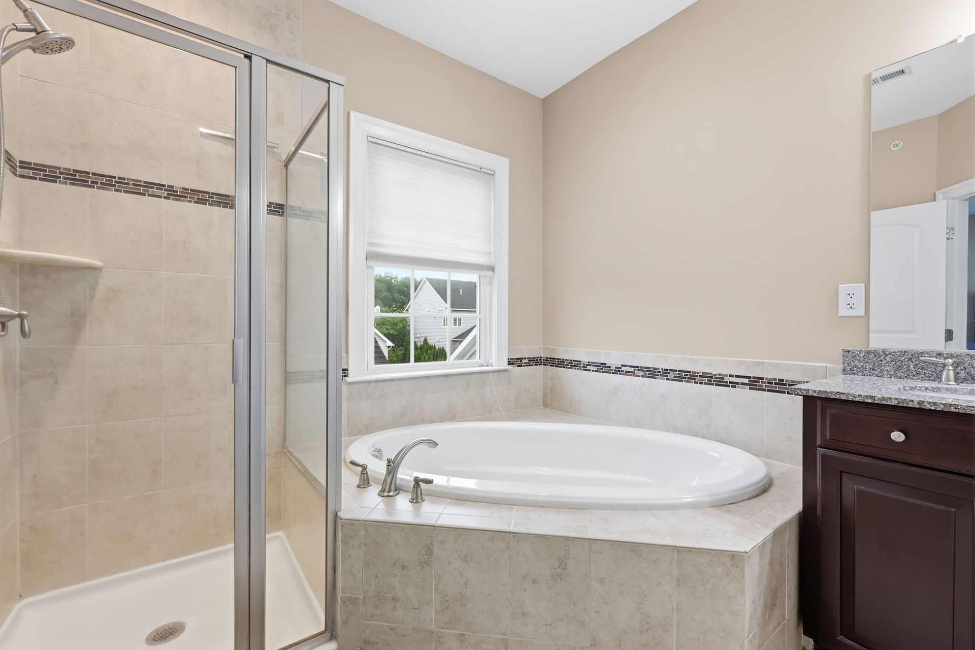 Bright bathroom with a corner soaking tub, glass shower, window, and dark wood vanity