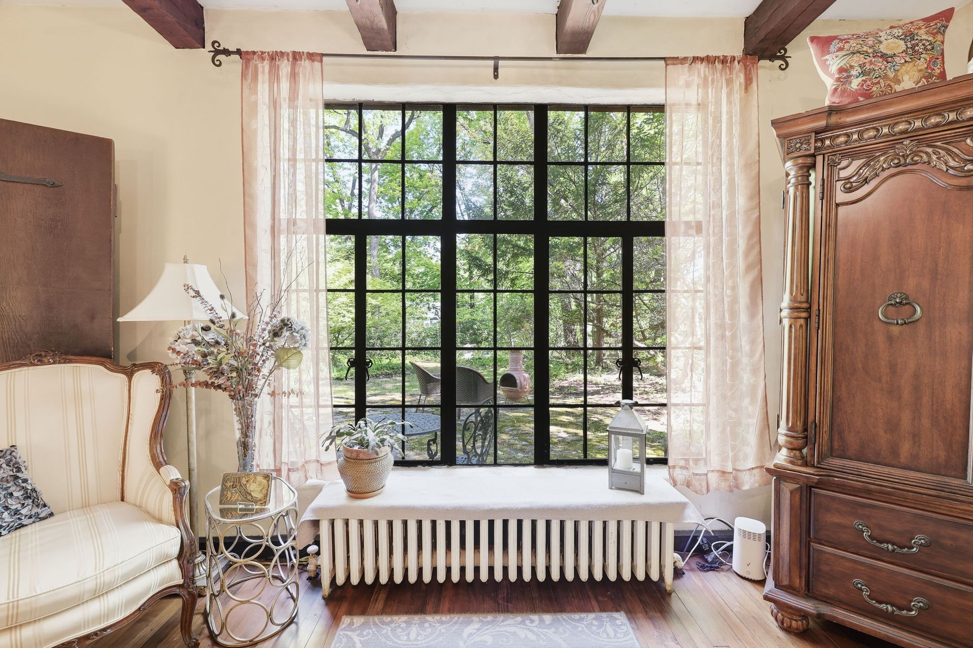 Bright living room with a large window, white curtains, sofa, and wooden cabinet