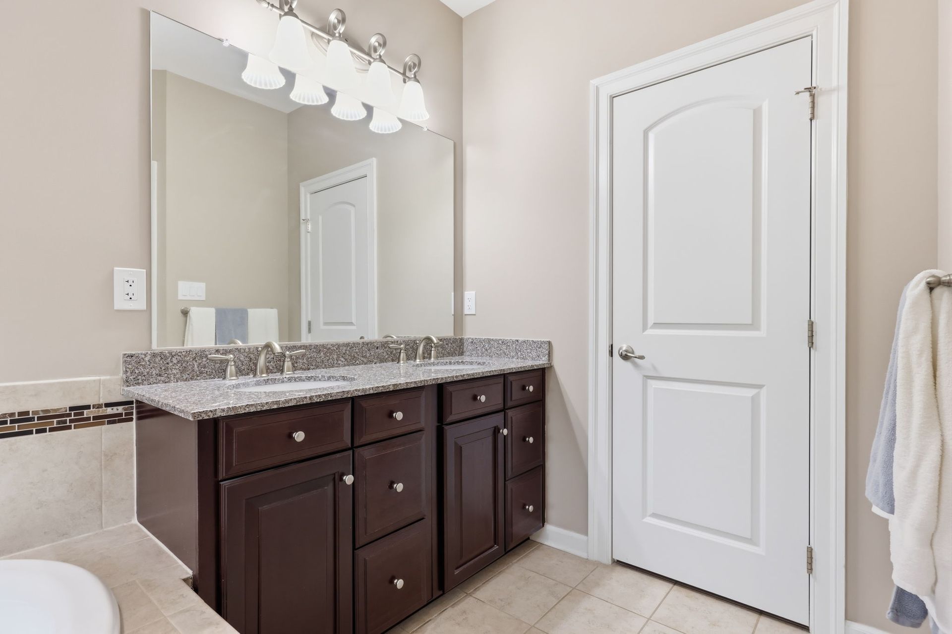Bathroom vanity with granite countertop, large mirror, white door, and dark wood cabinets