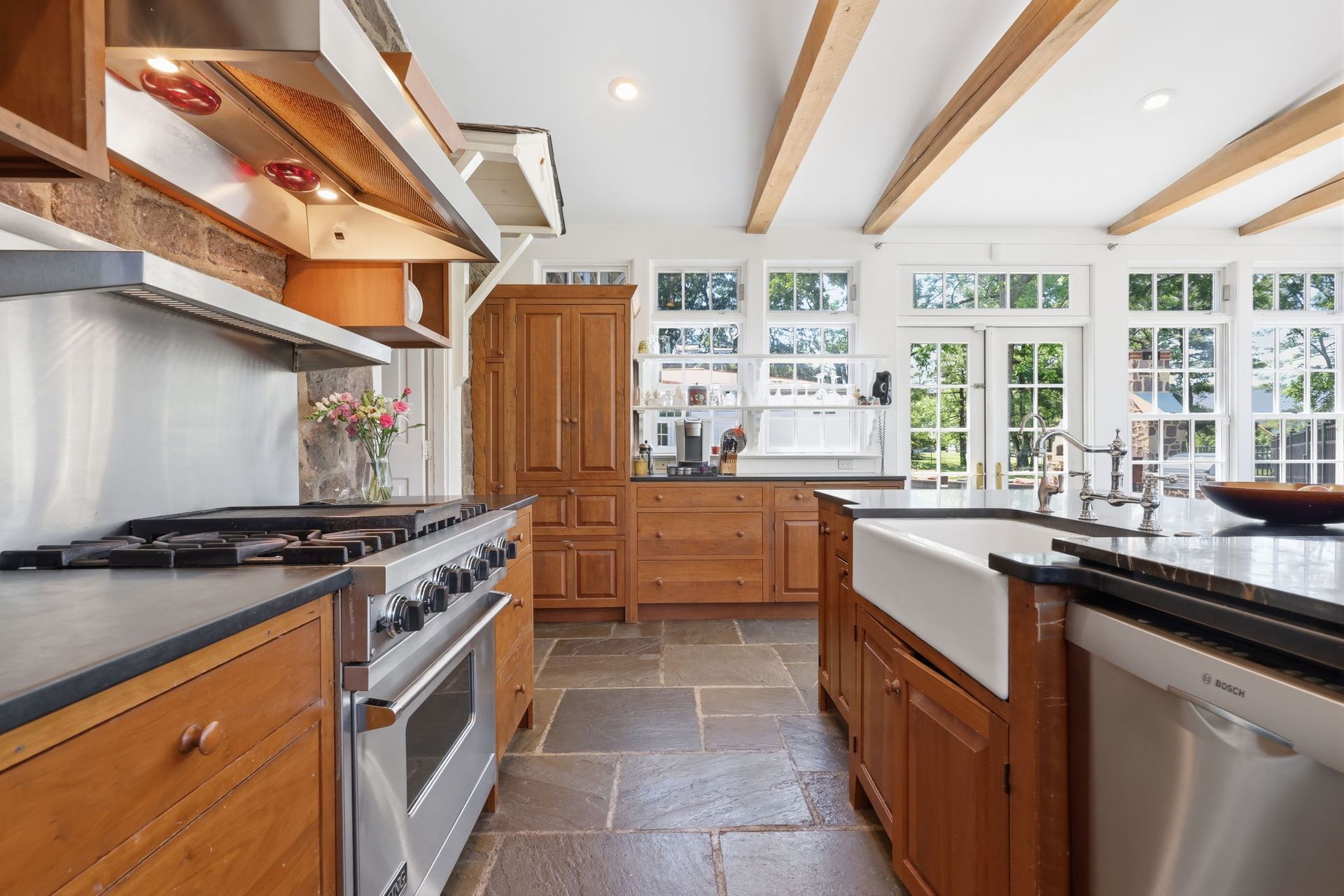 Bright modern kitchen with wood cabinets, stone floor, gas range, island sink, and sunlit windows