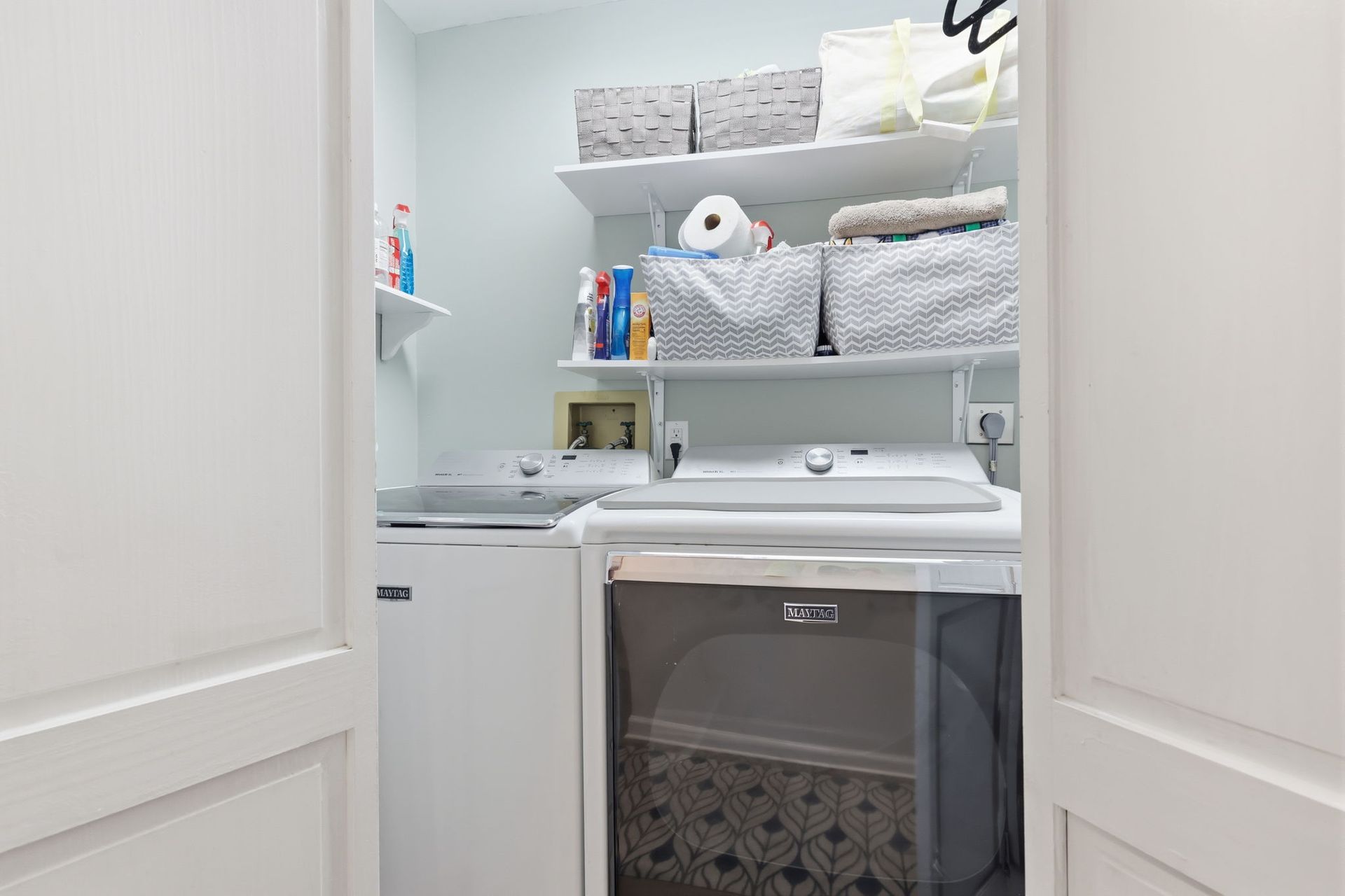 Compact laundry room with stacked washer and dryer, white cabinets, and shelves of toiletries