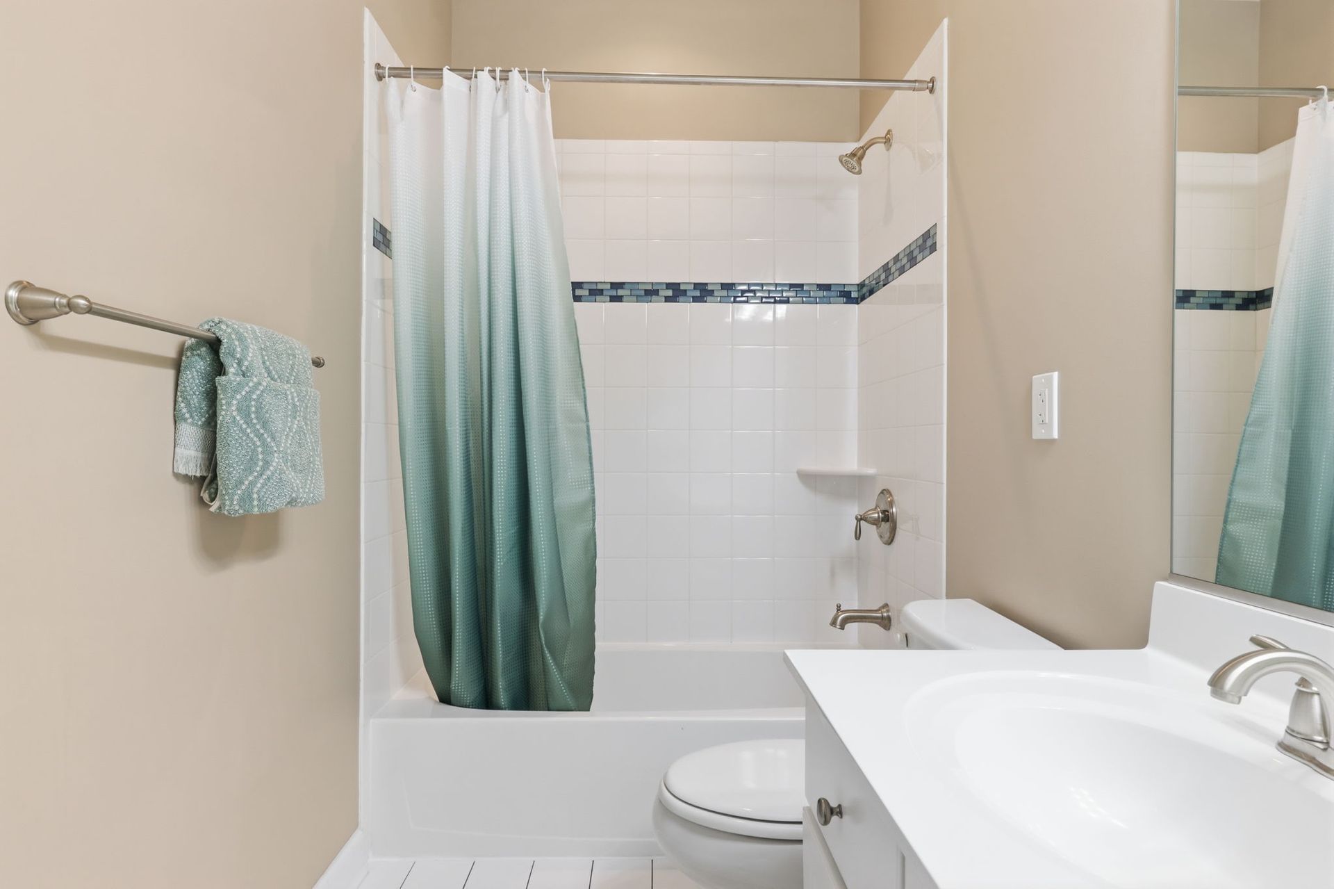 White bathroom with teal shower curtain, tiled shower, towel rack, and sink vanity.