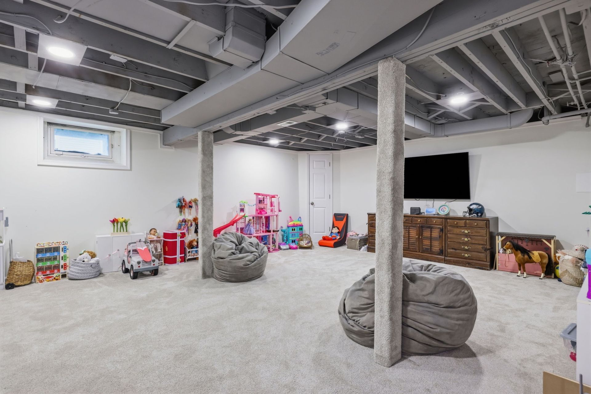 Spacious playroom with toys, bean bags, and a TV on a white carpeted floor