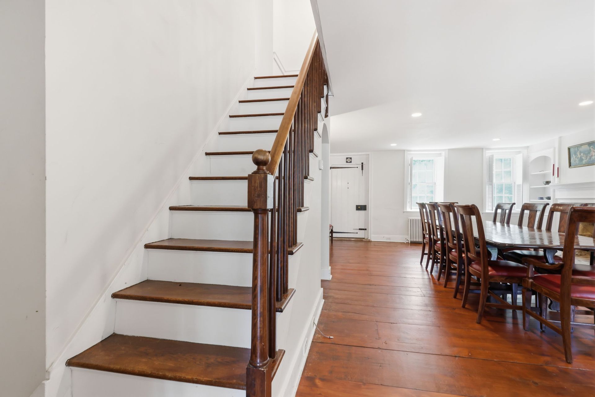Staircase beside an open dining area with hardwood floors and a long table and chairs