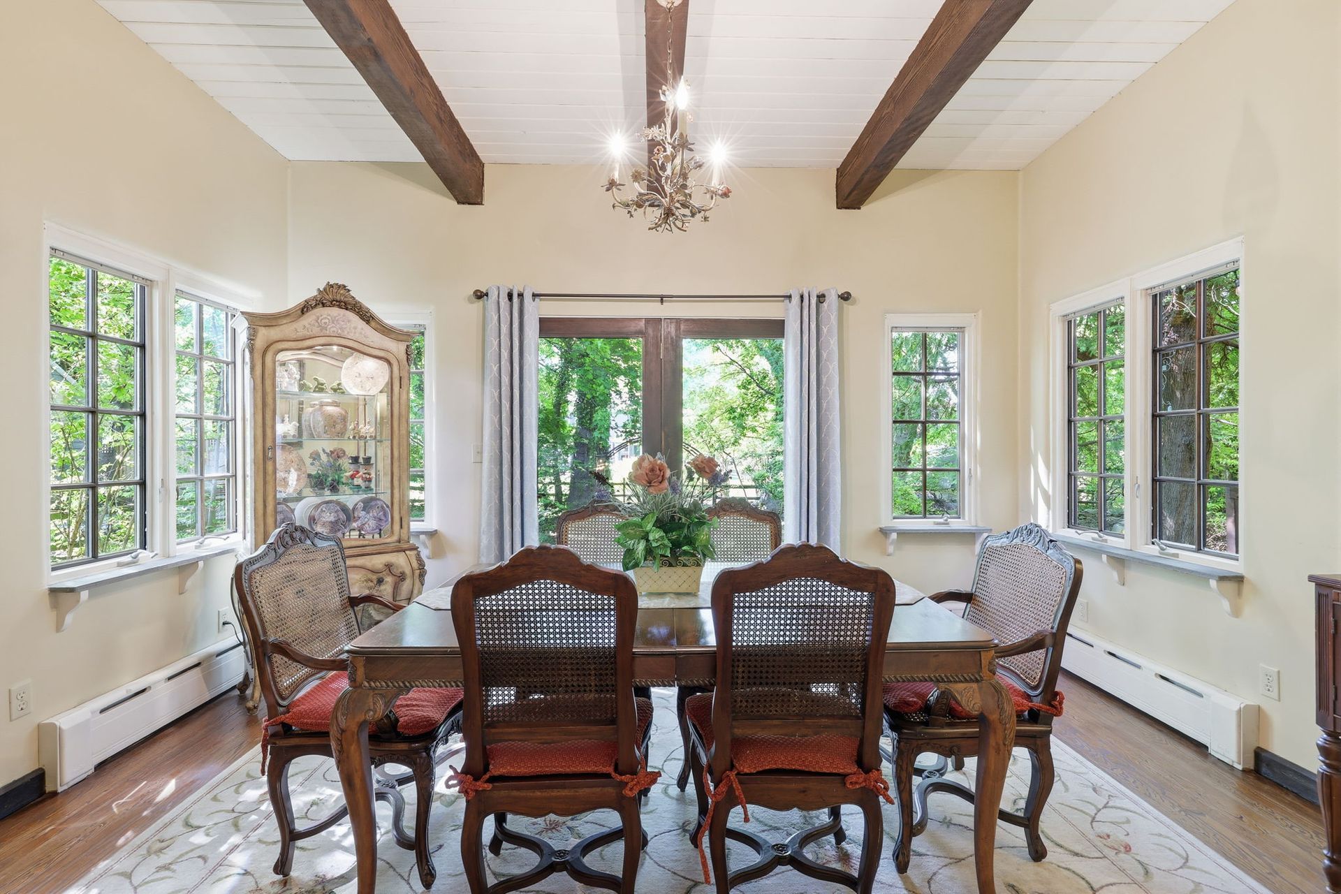 Bright dining room with wooden table and chairs, large windows, chandelier, and garden view
