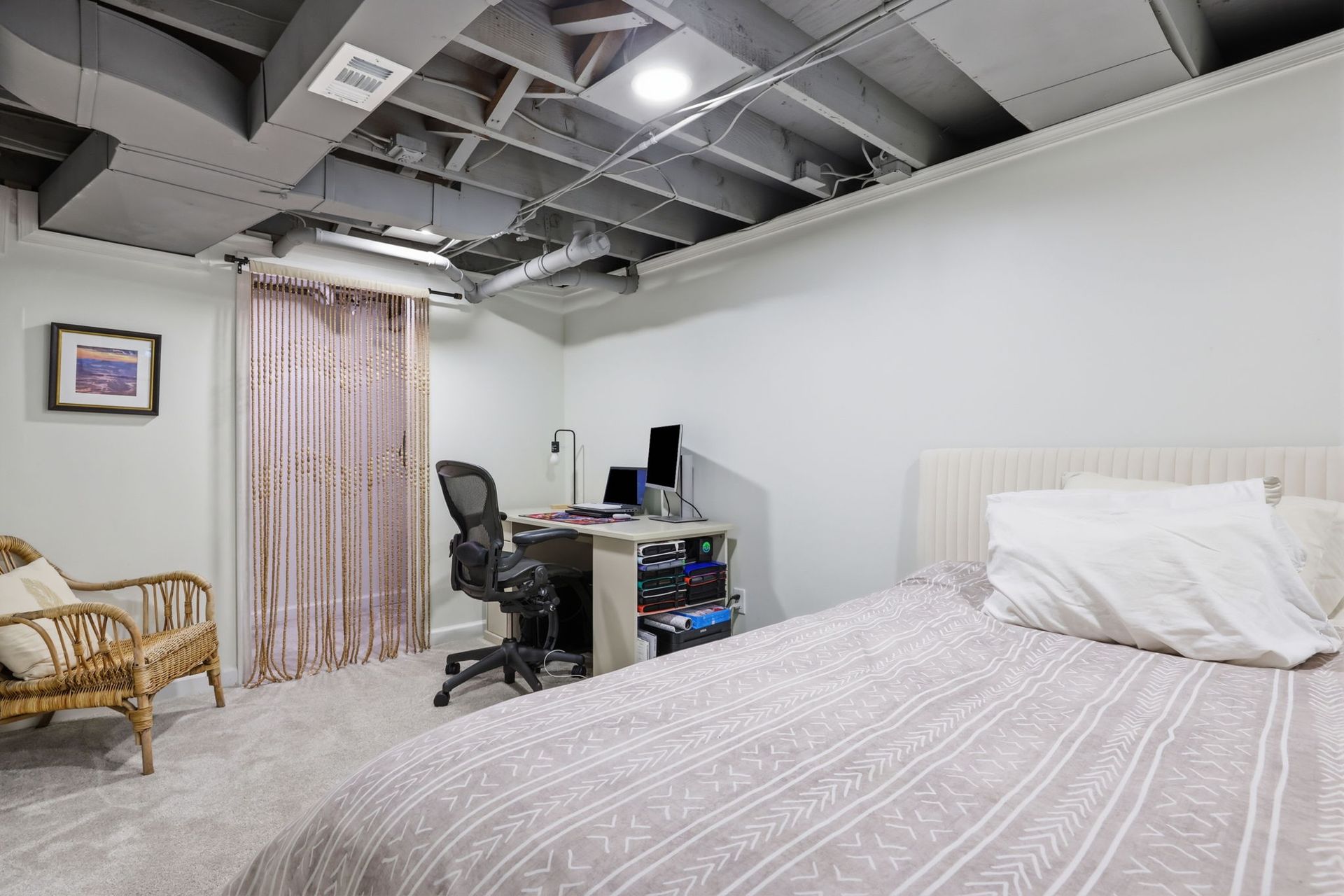 Bedroom with bed, desk, chair, wicker seating, and exposed ceiling beams